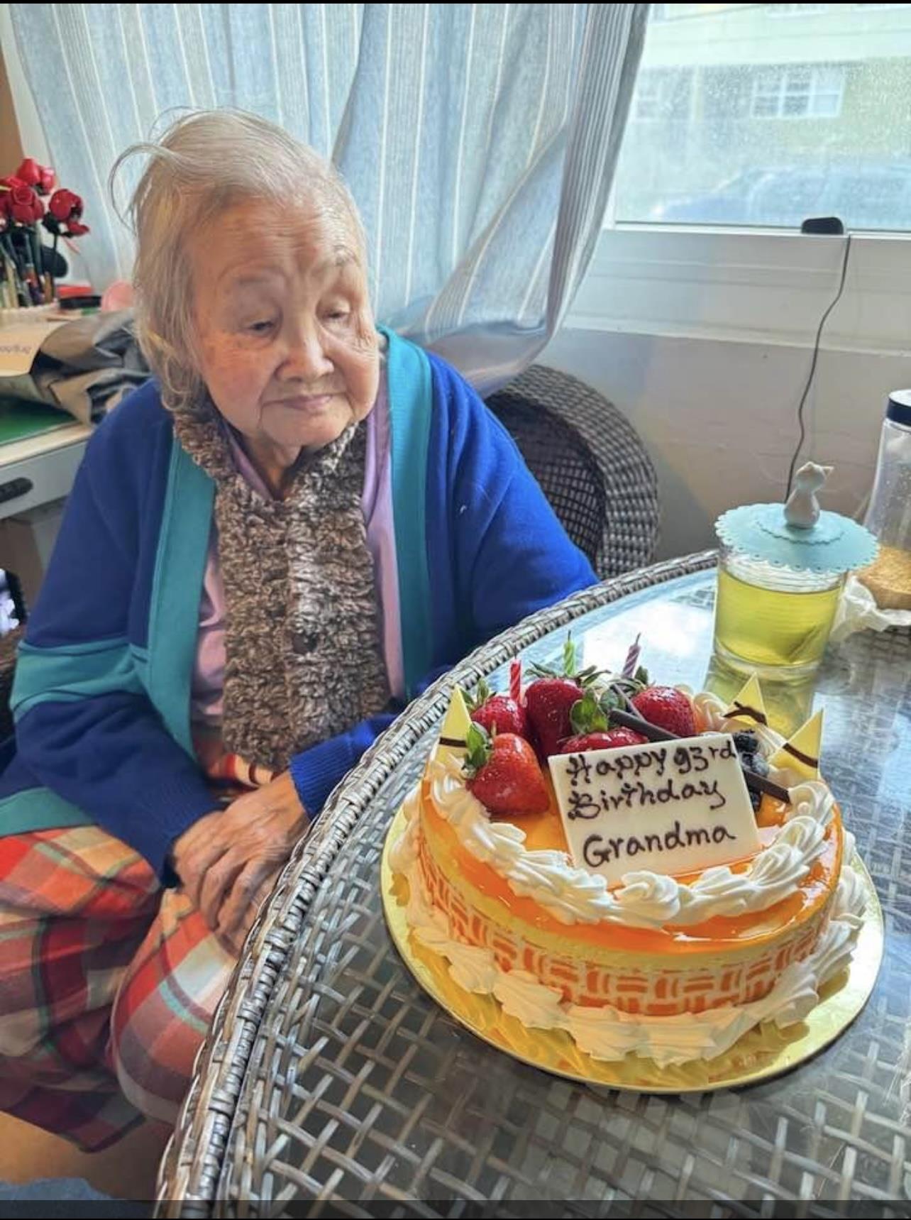 An old woman sitting in front of a cake