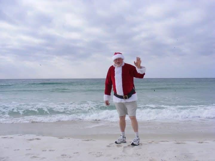 A man in a santa garment waving at the beach