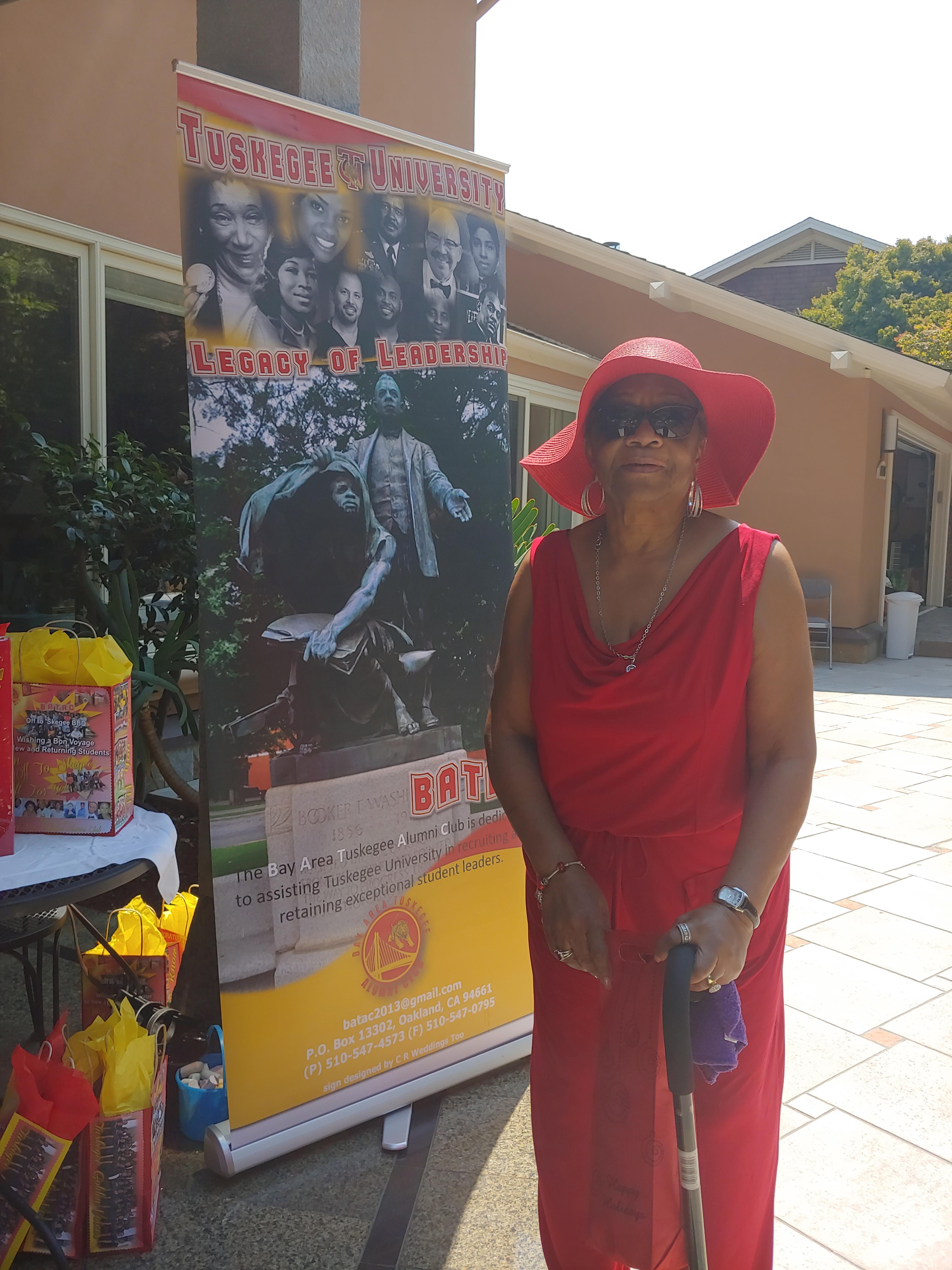 A woman in a red dress and hat standing in front of a sign