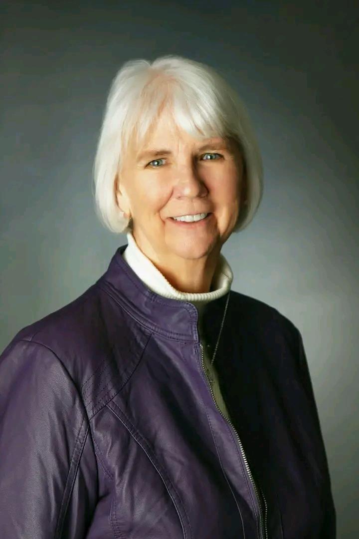 A woman with white hair wearing a purple jacket