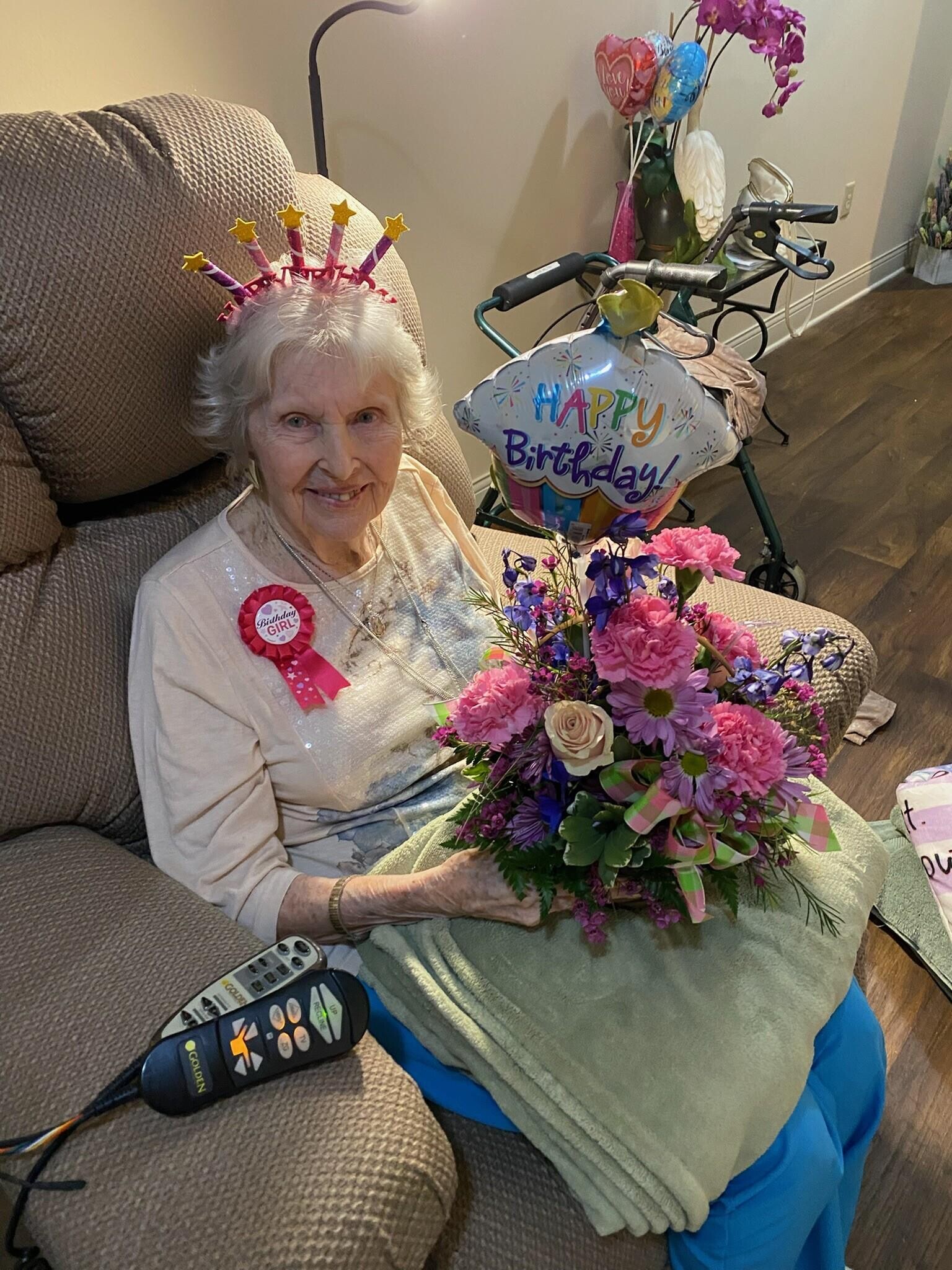 An old woman sitting on a couch holding a bouquet of flowers
