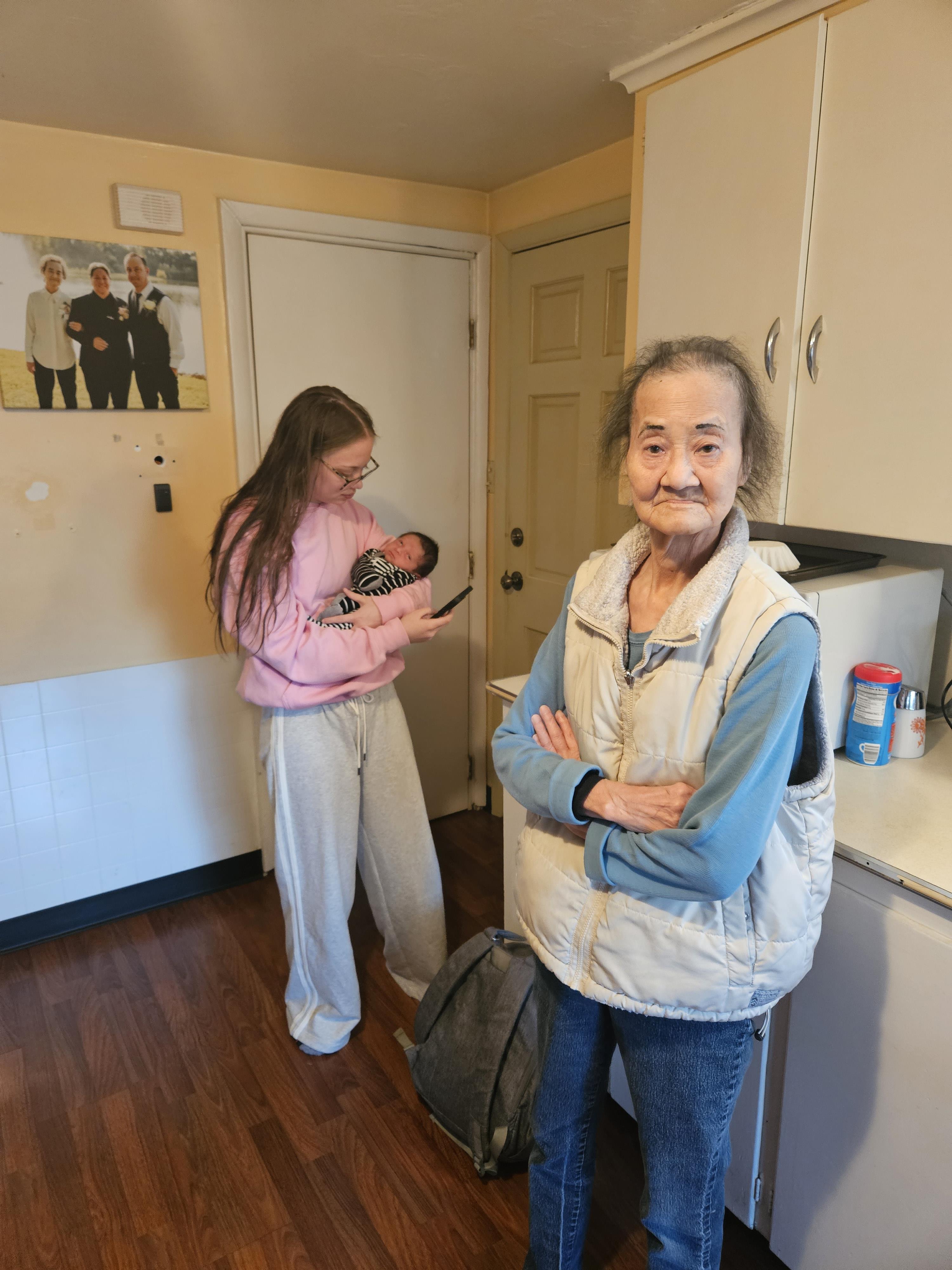 A woman standing in a kitchen with a baby and a woman holding a baby