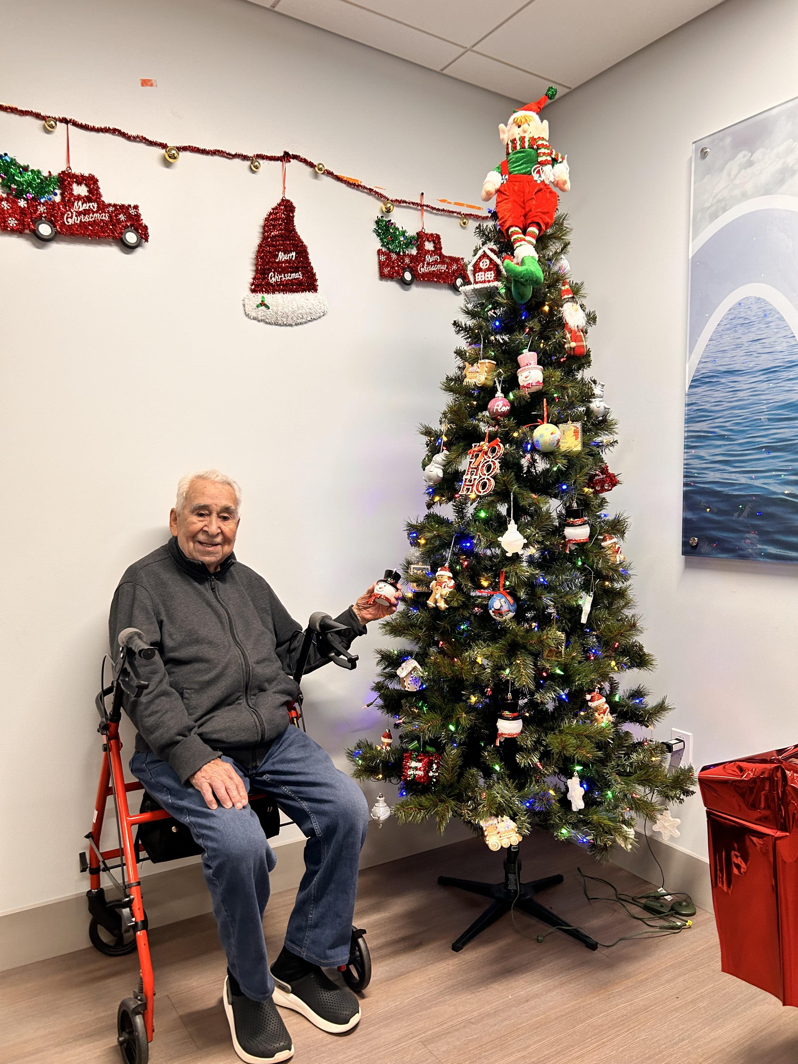 A man sitting in a wheelchair next to a christmas tree