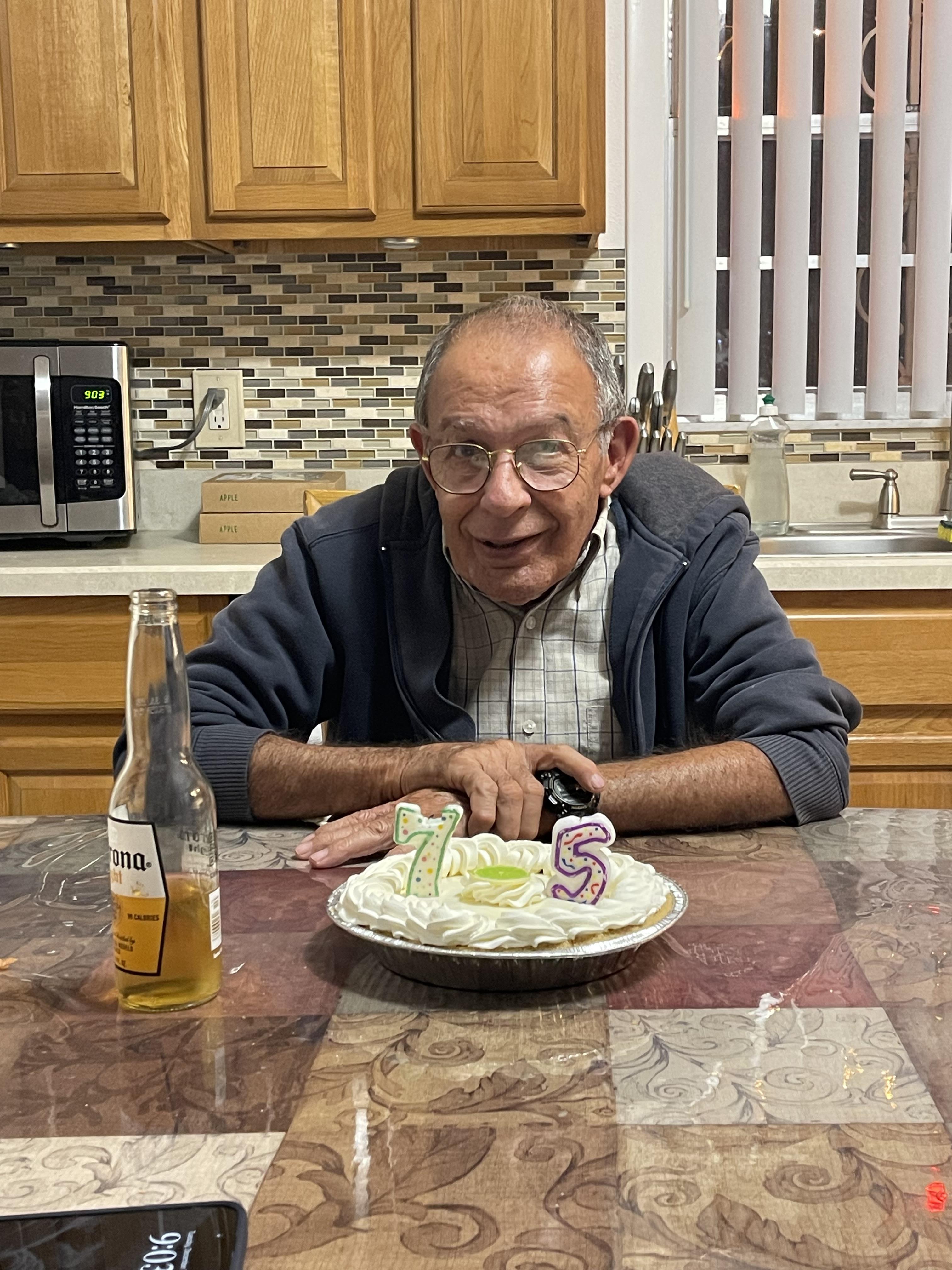 A man sitting at a table with a cake and a bottle of beer