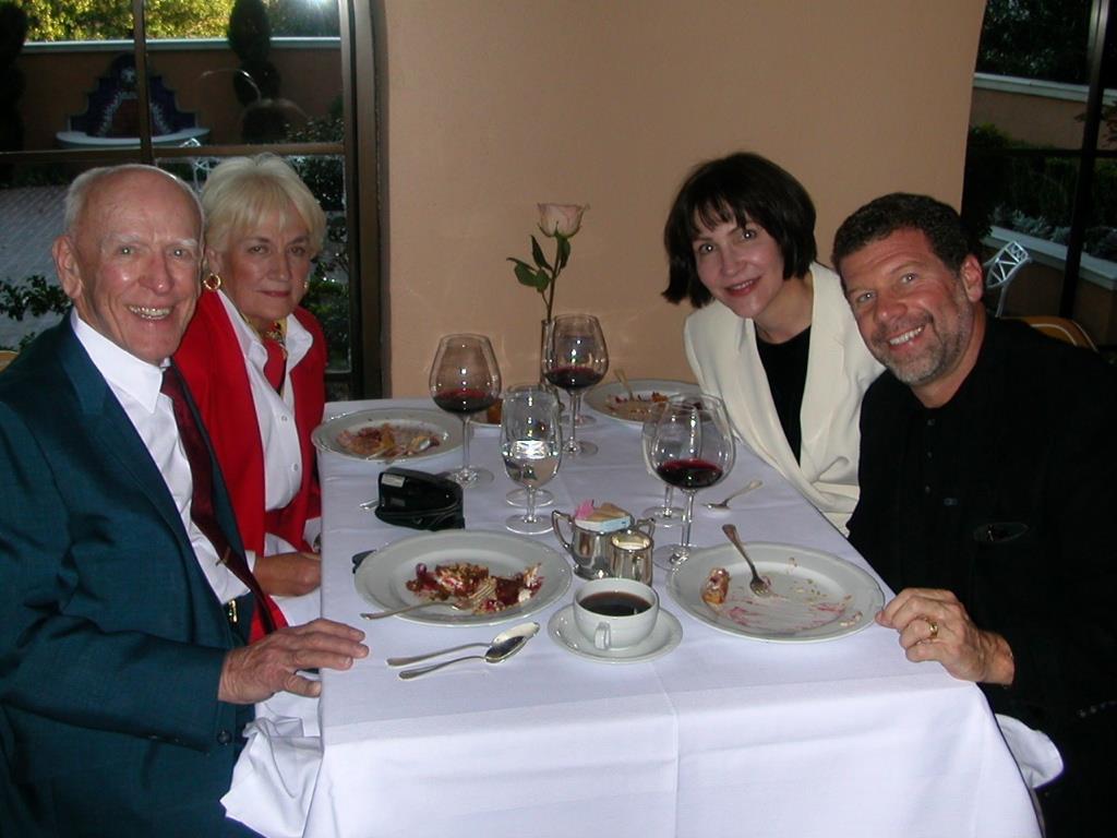 A group of people sitting at a table with plates of food and wine