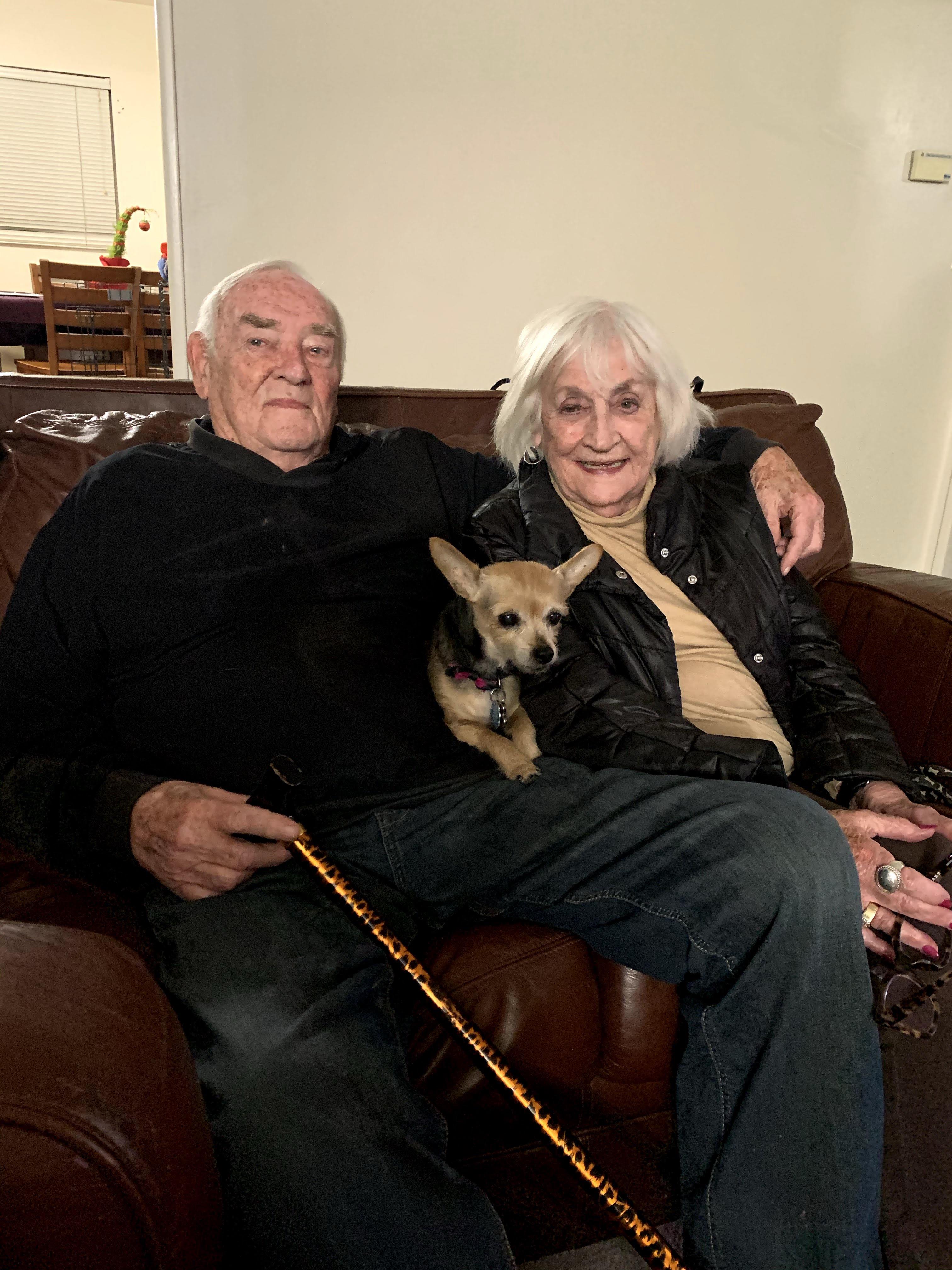 A man and woman sitting on a couch with a dog