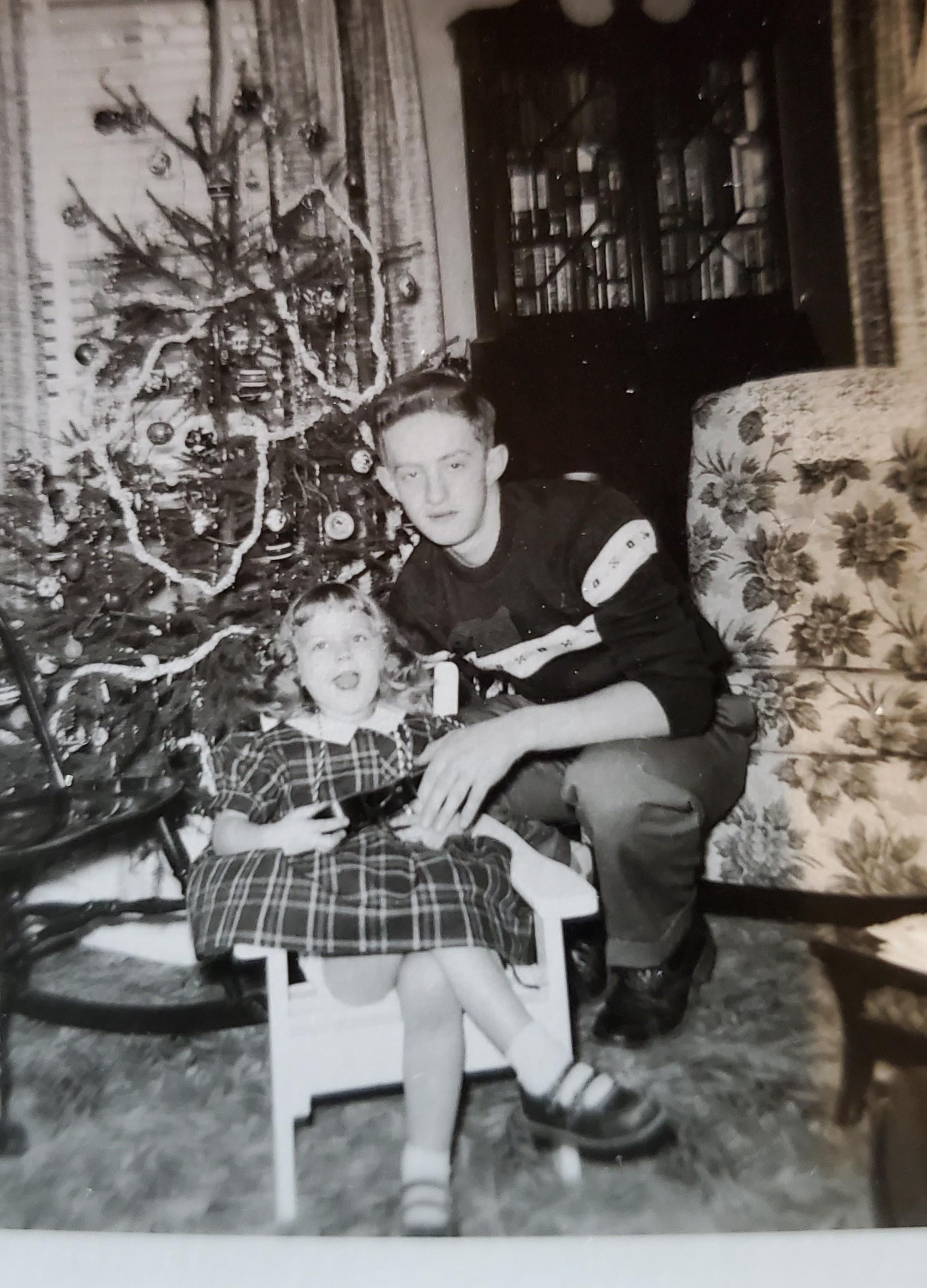 A man and a girl sitting in a chair next to a christmas tree