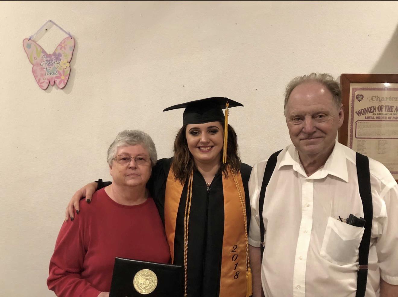 A woman in a graduation cap and gown with a man and woman in a room