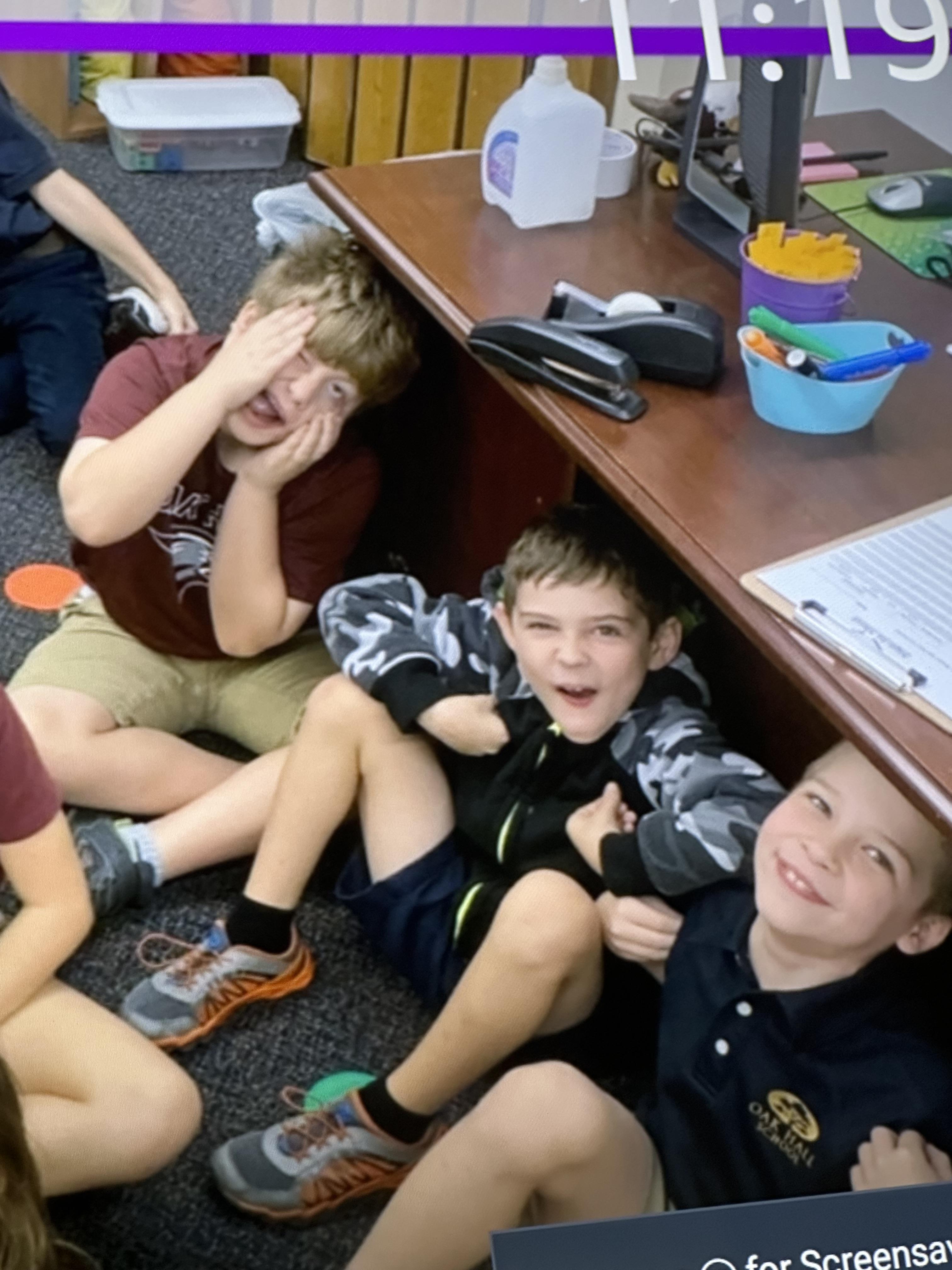 A group of boys sitting under a desk