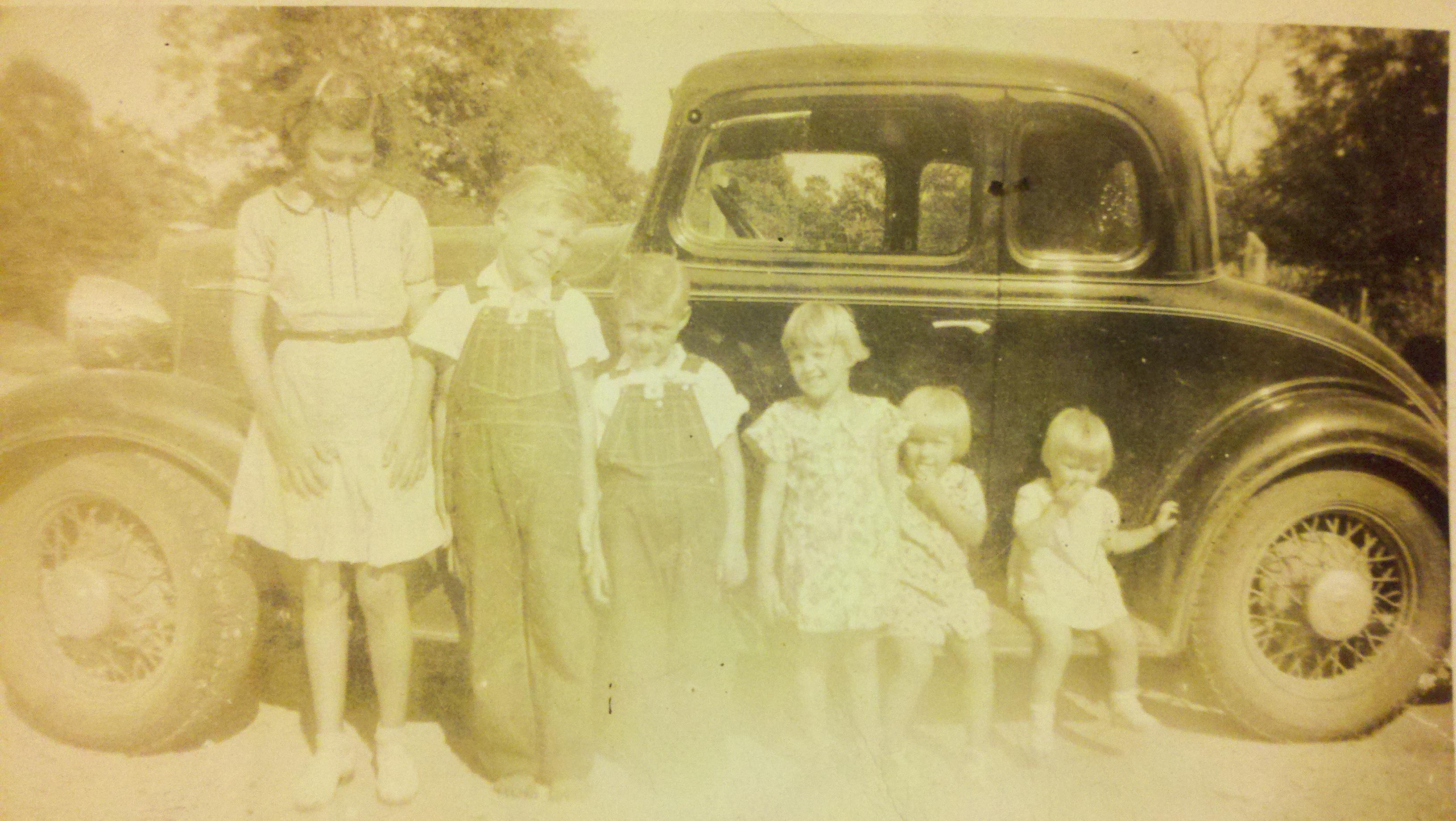 A group of children standing in front of a car