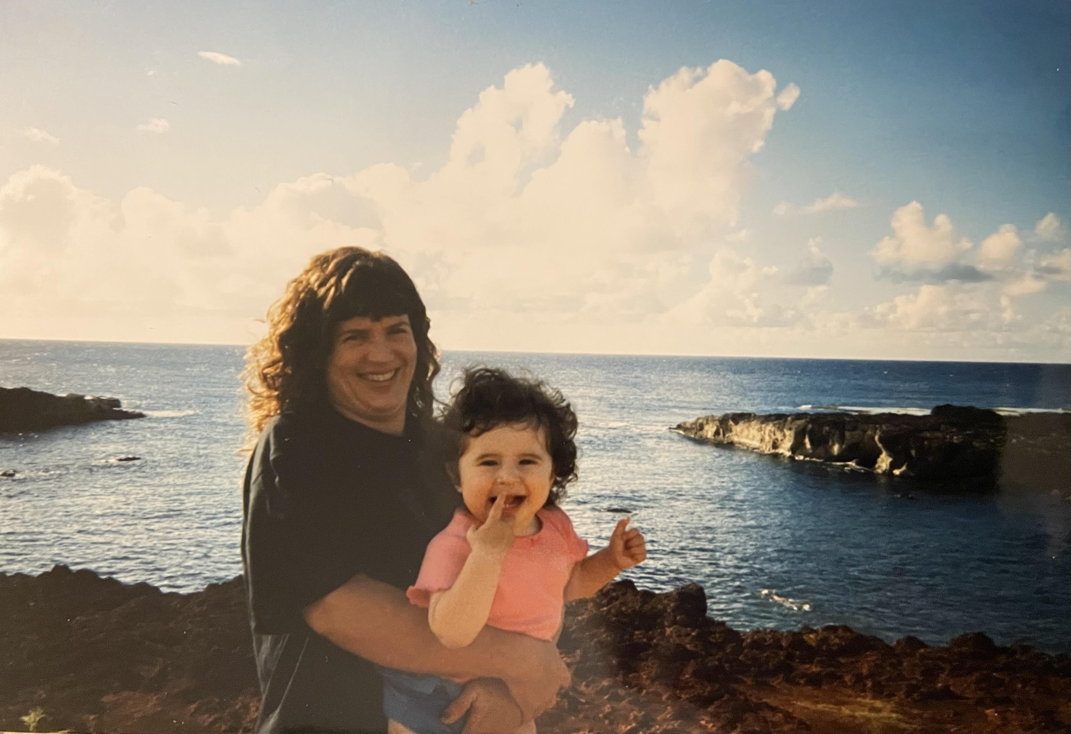 A woman holding a baby by the water