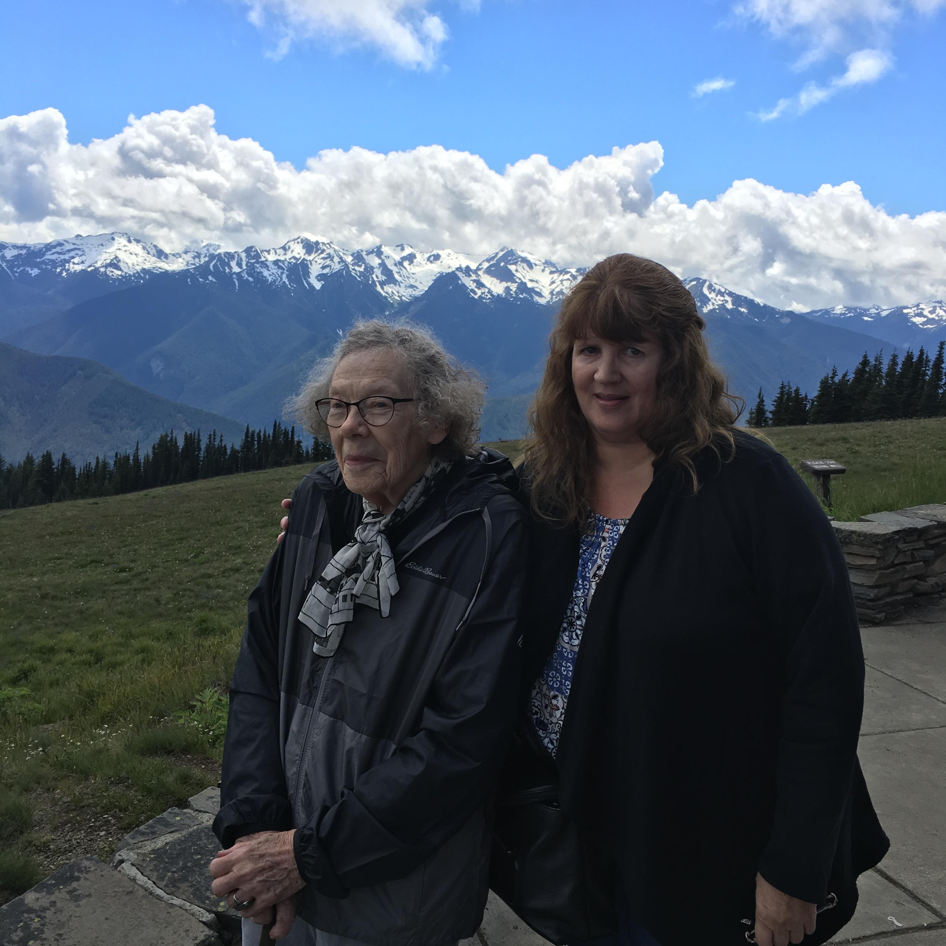 Two women standing on a ledge with mountains in the background