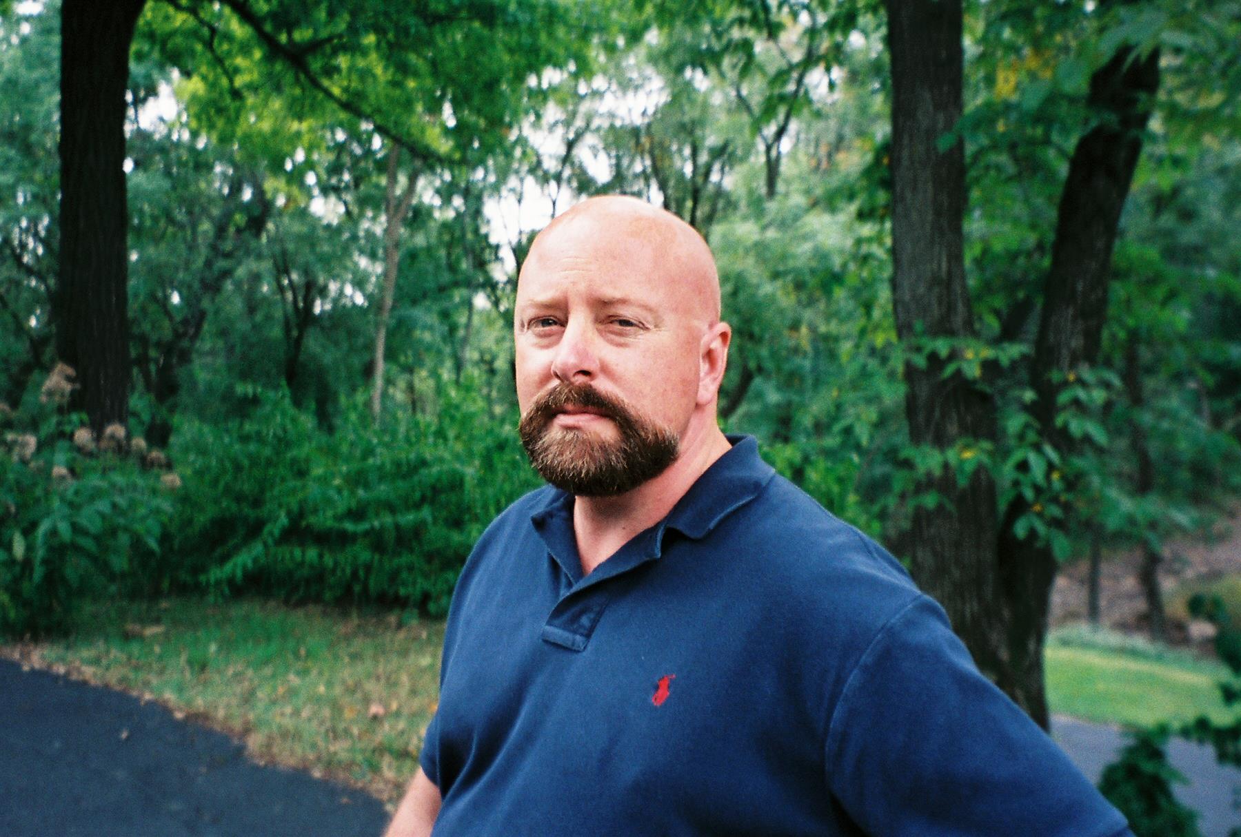 A man with a beard and mustache standing in a park