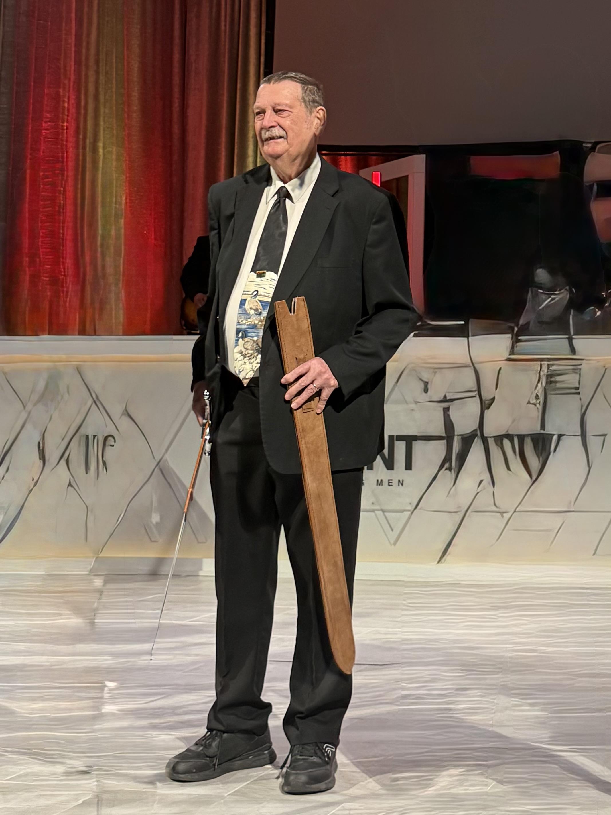 A man in a suit holding a wooden sword