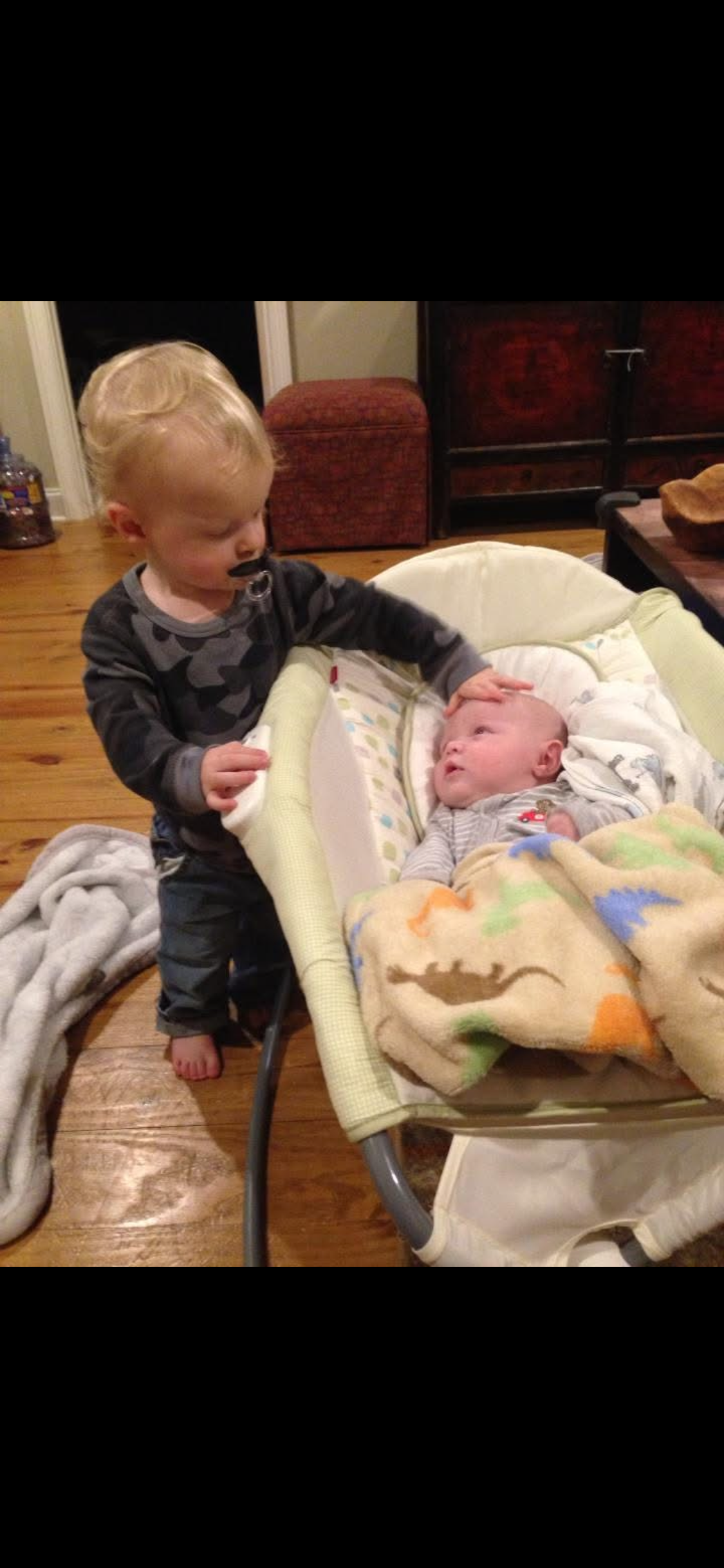A baby standing next to a baby in a cradle