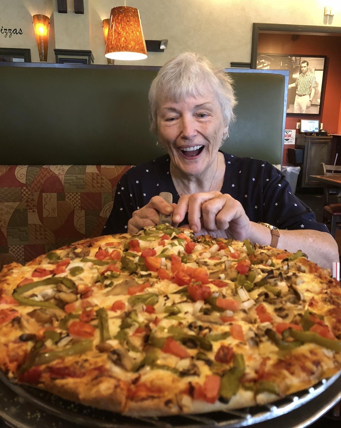 A woman sitting at a table with a large pizza