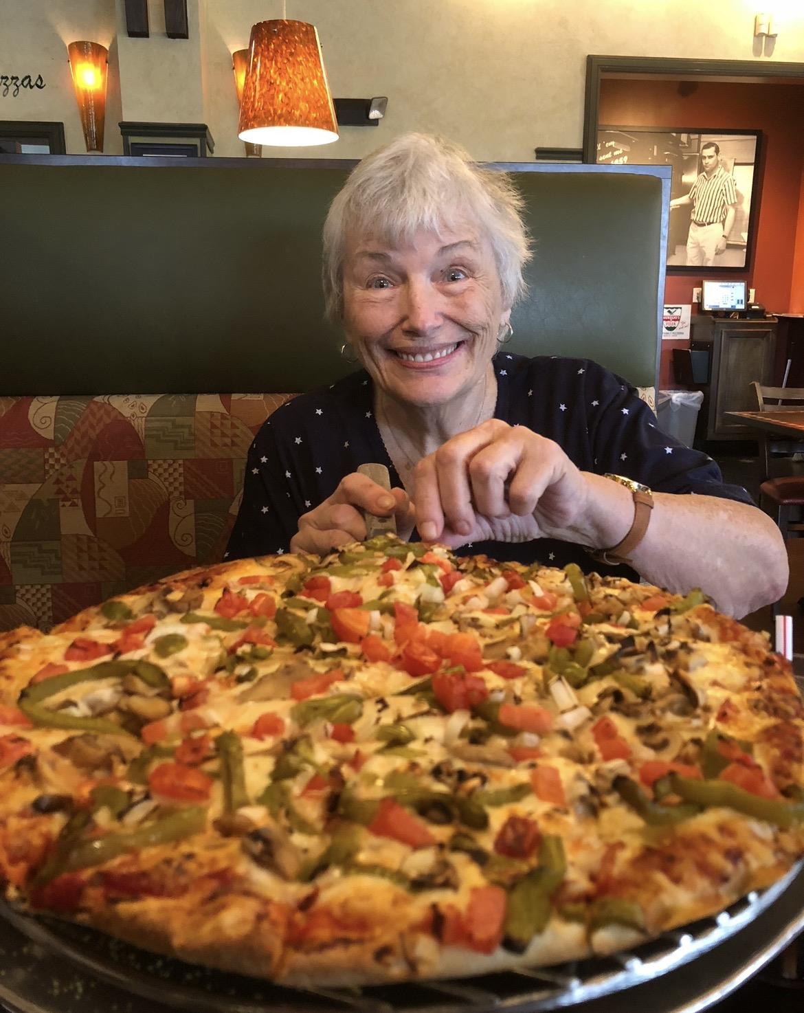 A woman sitting in a chair with a large pizza