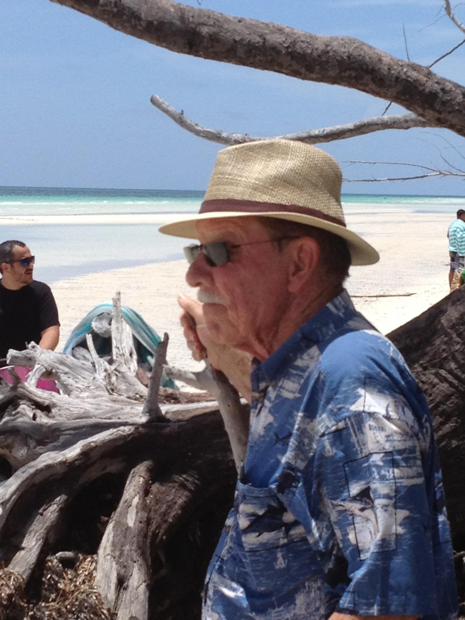 A man in a hat and sunglasses sitting on a beach