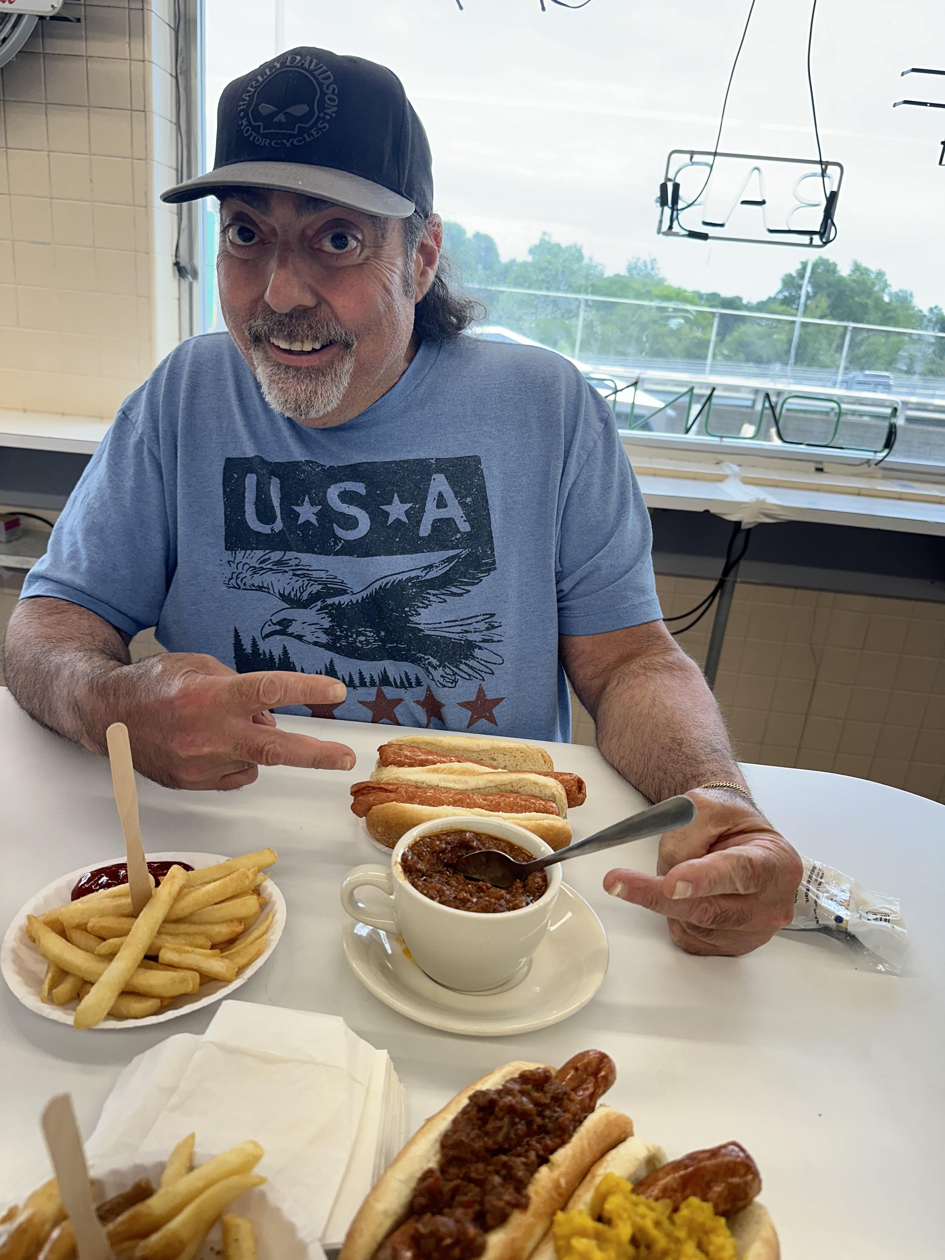 A man sitting at a table with hot dogs and a cup of soup