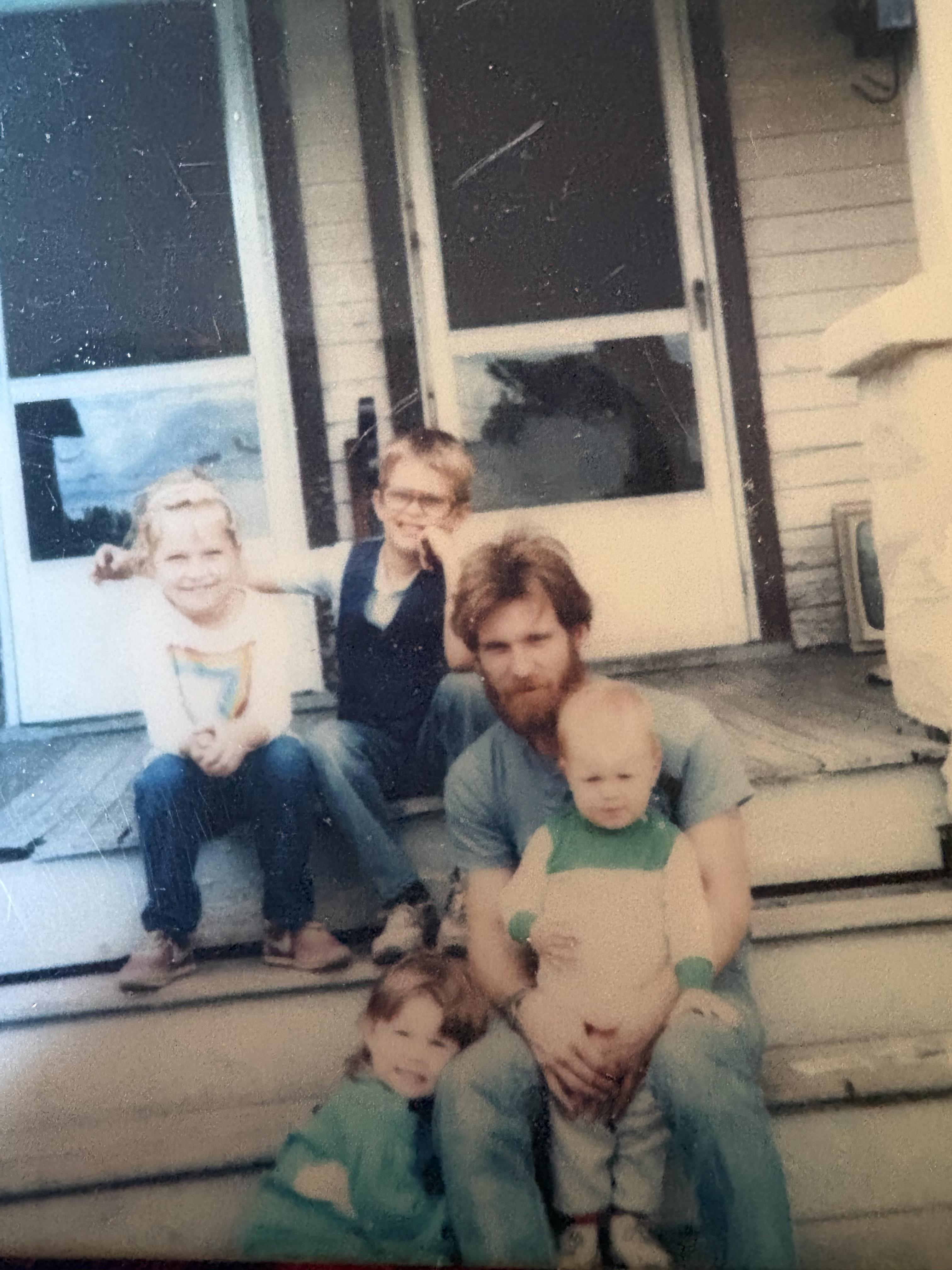 A man holding a baby and a group of children sitting on a porch