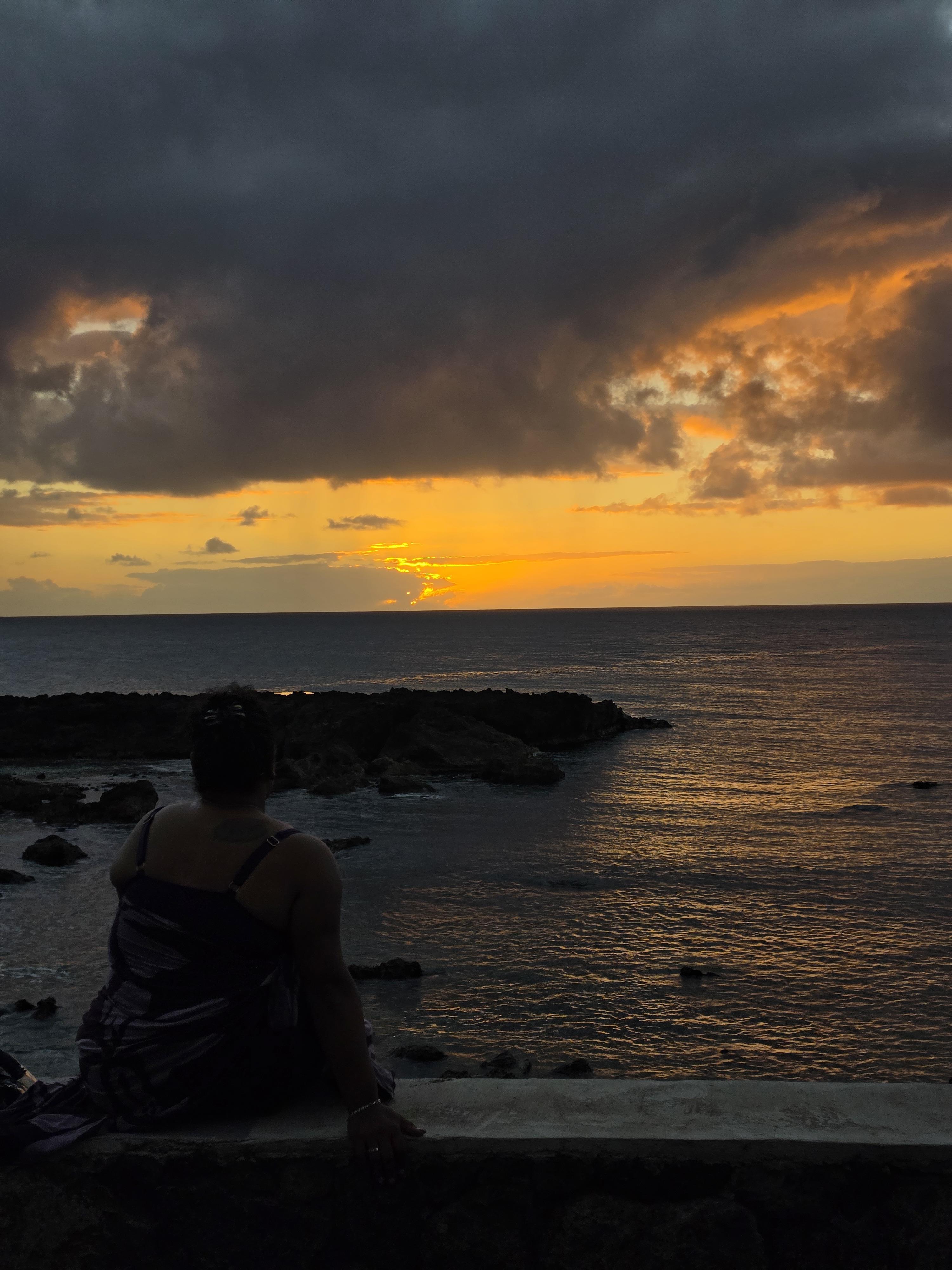 A person sitting on a rock looking at the sunset