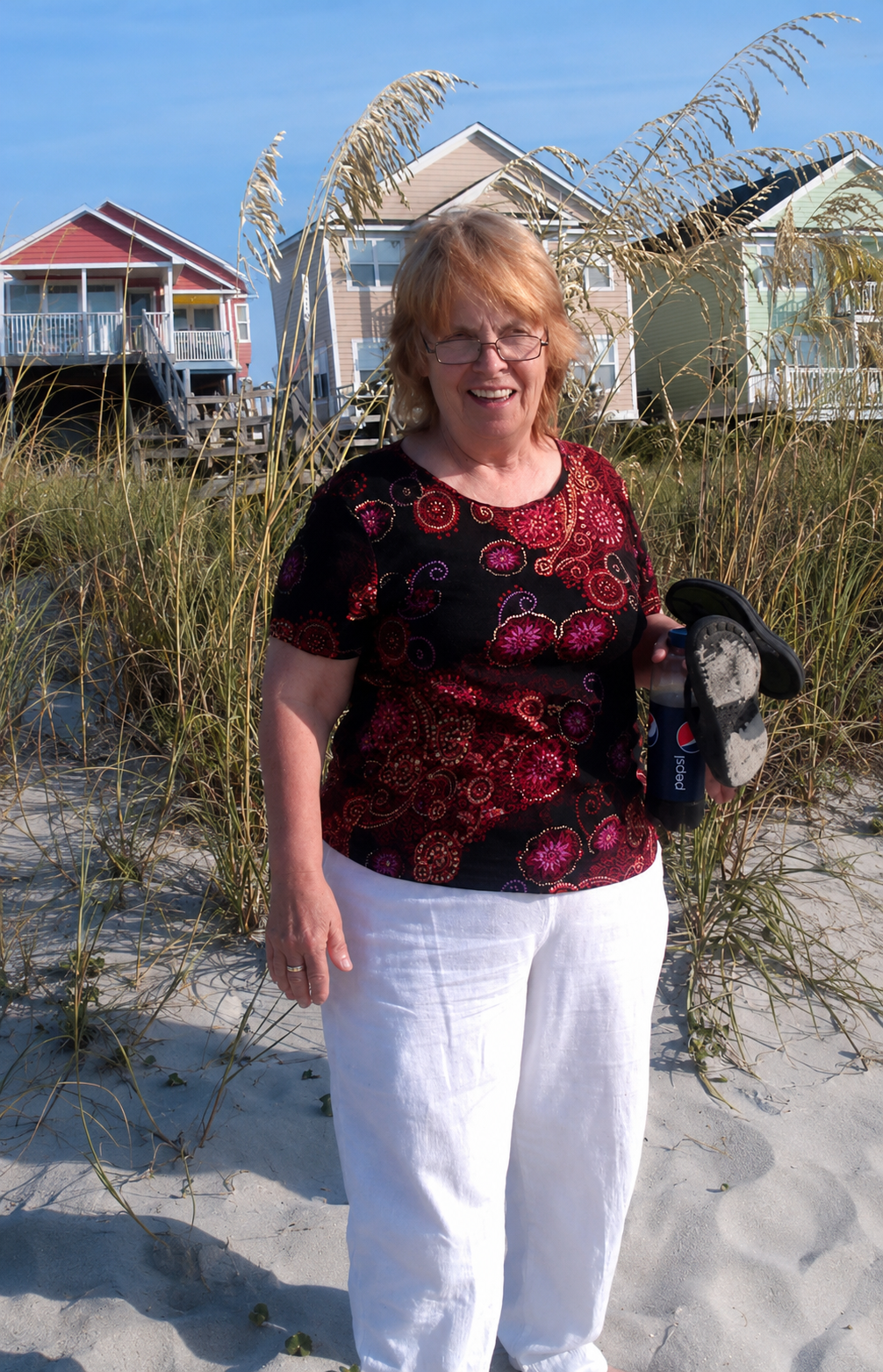 A woman standing on a beach holding a bottle of soda and a water bottle