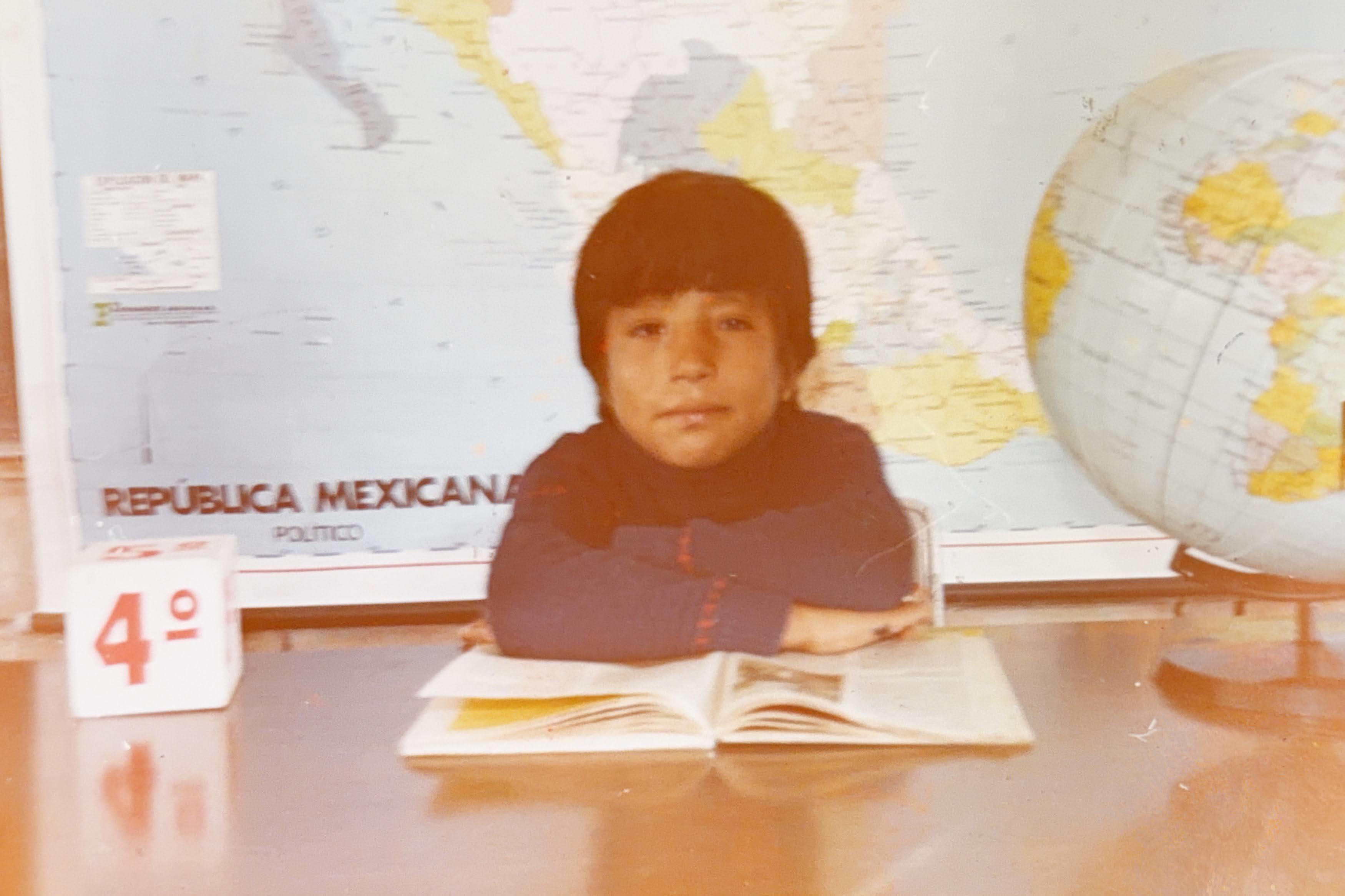 A boy sitting at a desk with a book and a globe behind him