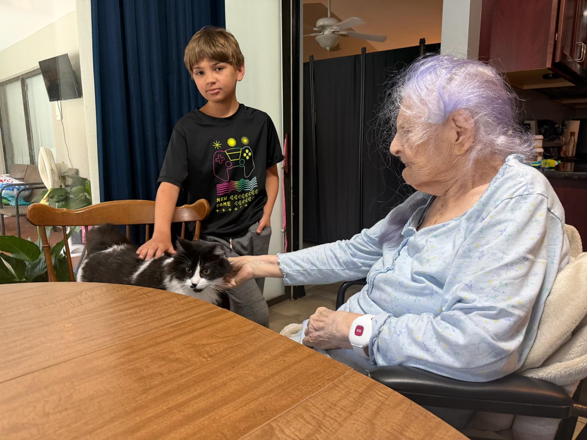 An old woman and a young boy sitting at a table with a cat