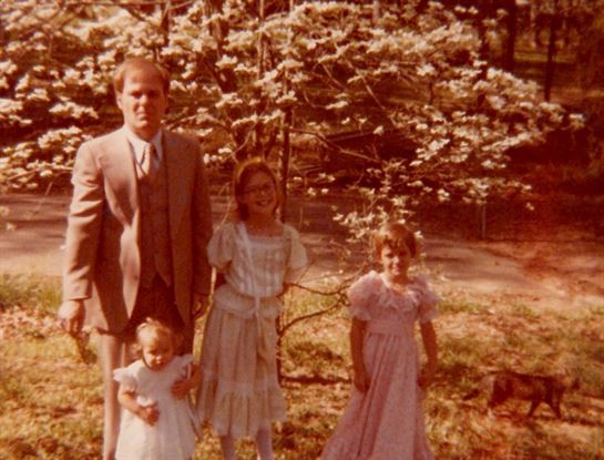 A man and two girls standing in front of a tree