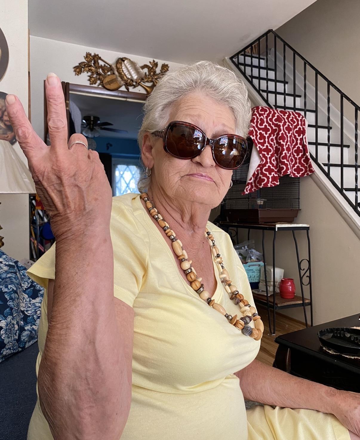 An old woman wearing sunglasses and holding up her hand