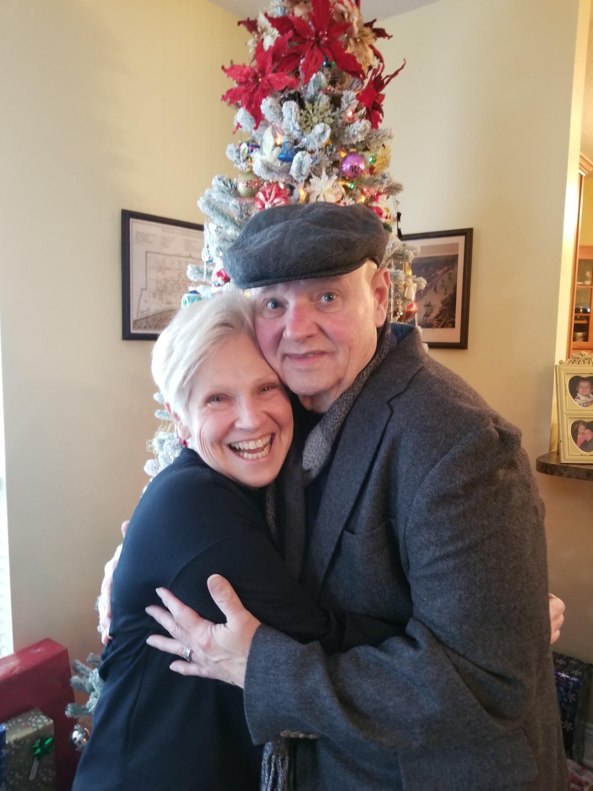 A man and woman hugging in front of a christmas tree