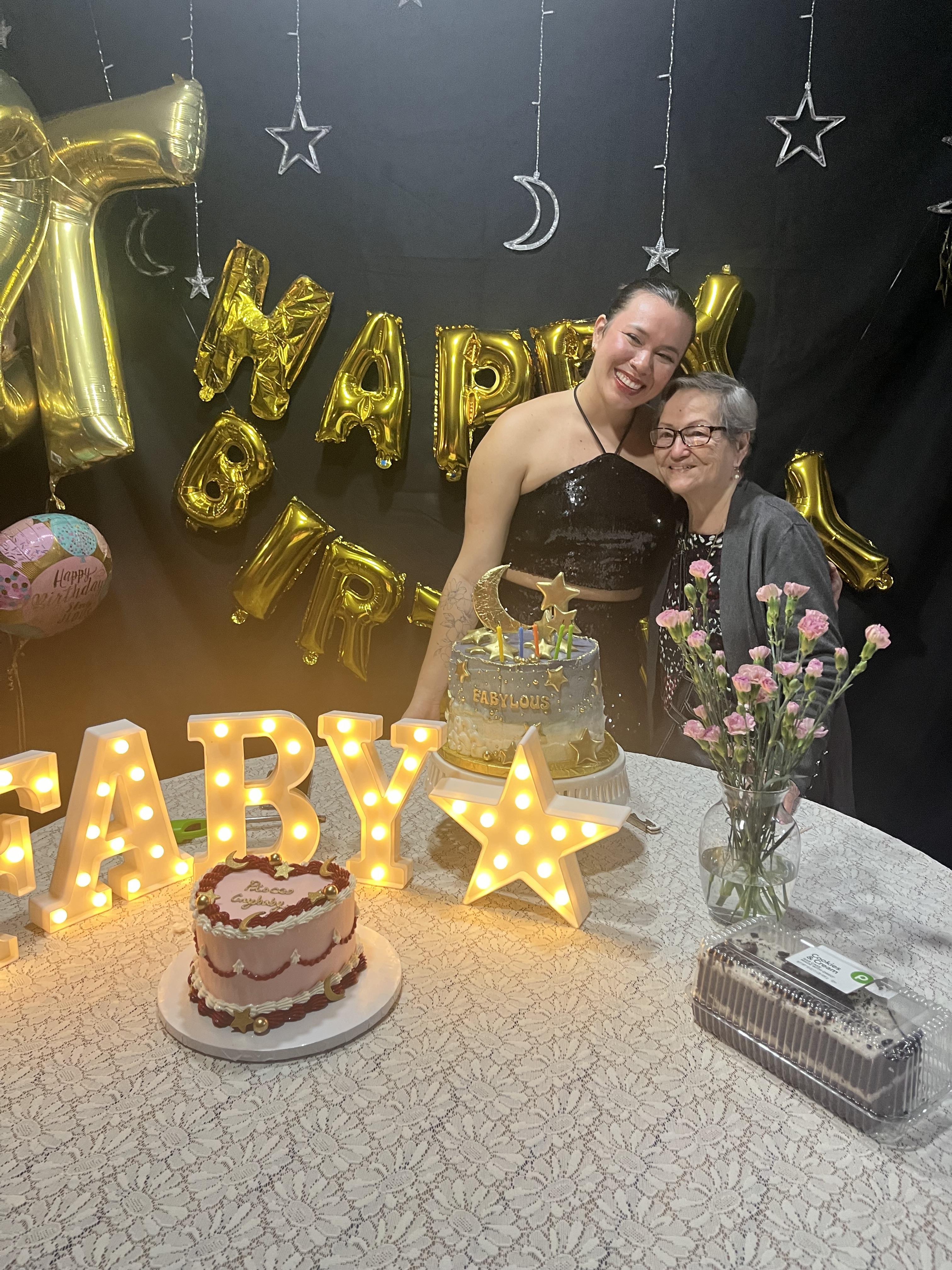 A woman standing next to a cake with a cake and balloons on a table