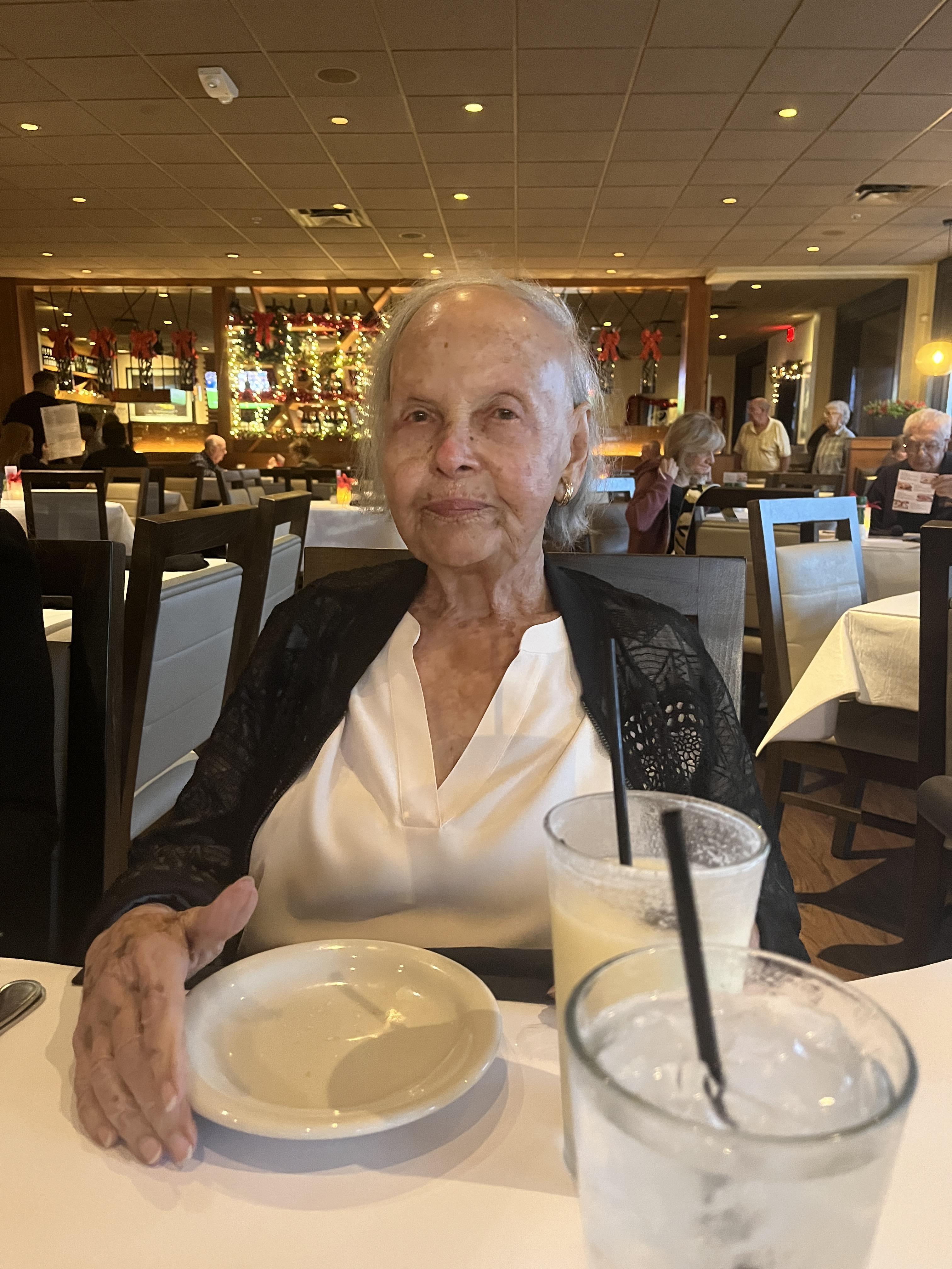An old woman sitting at a table with a plate and a drink