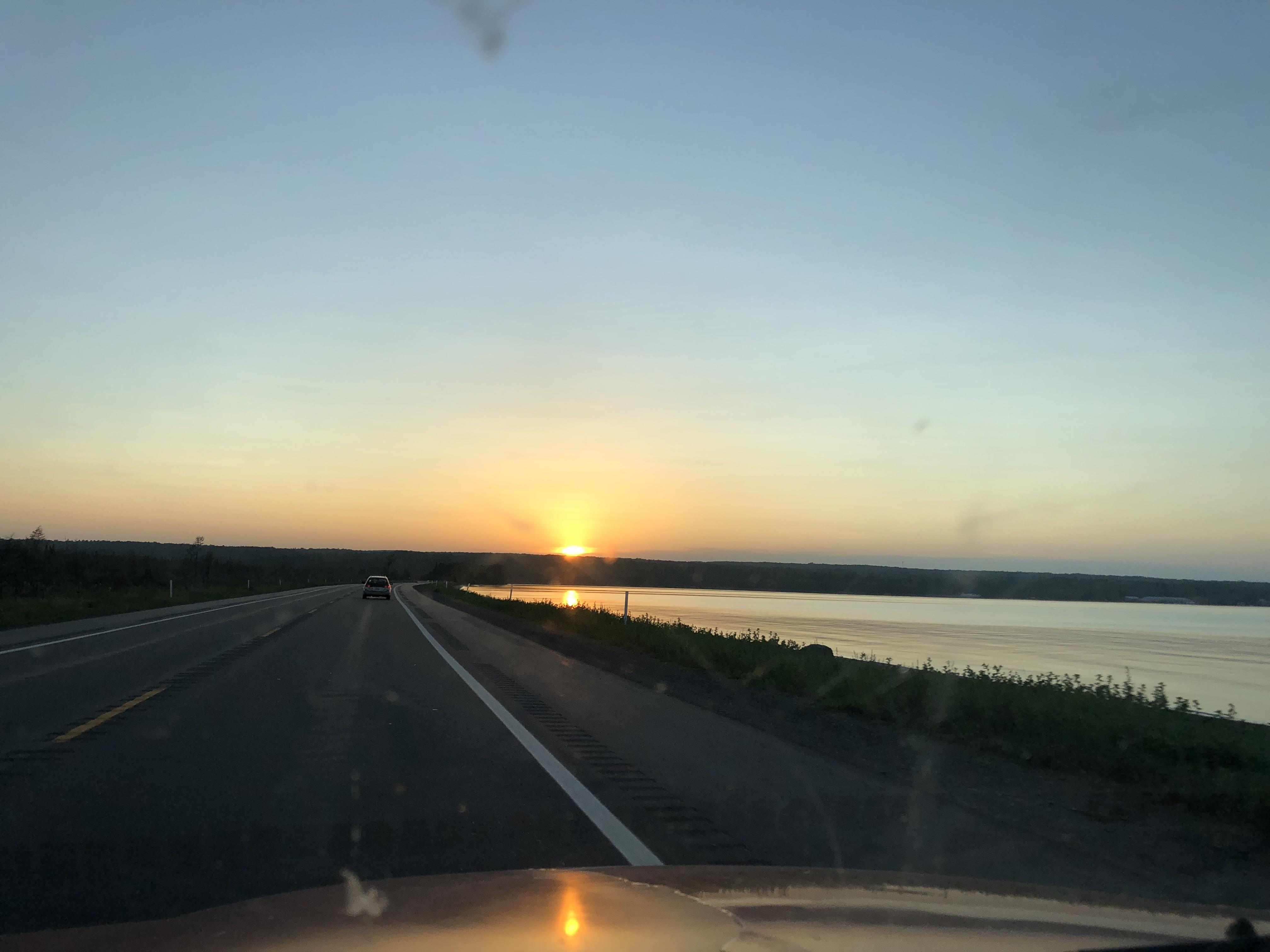 A road with a body of water and a sunset
