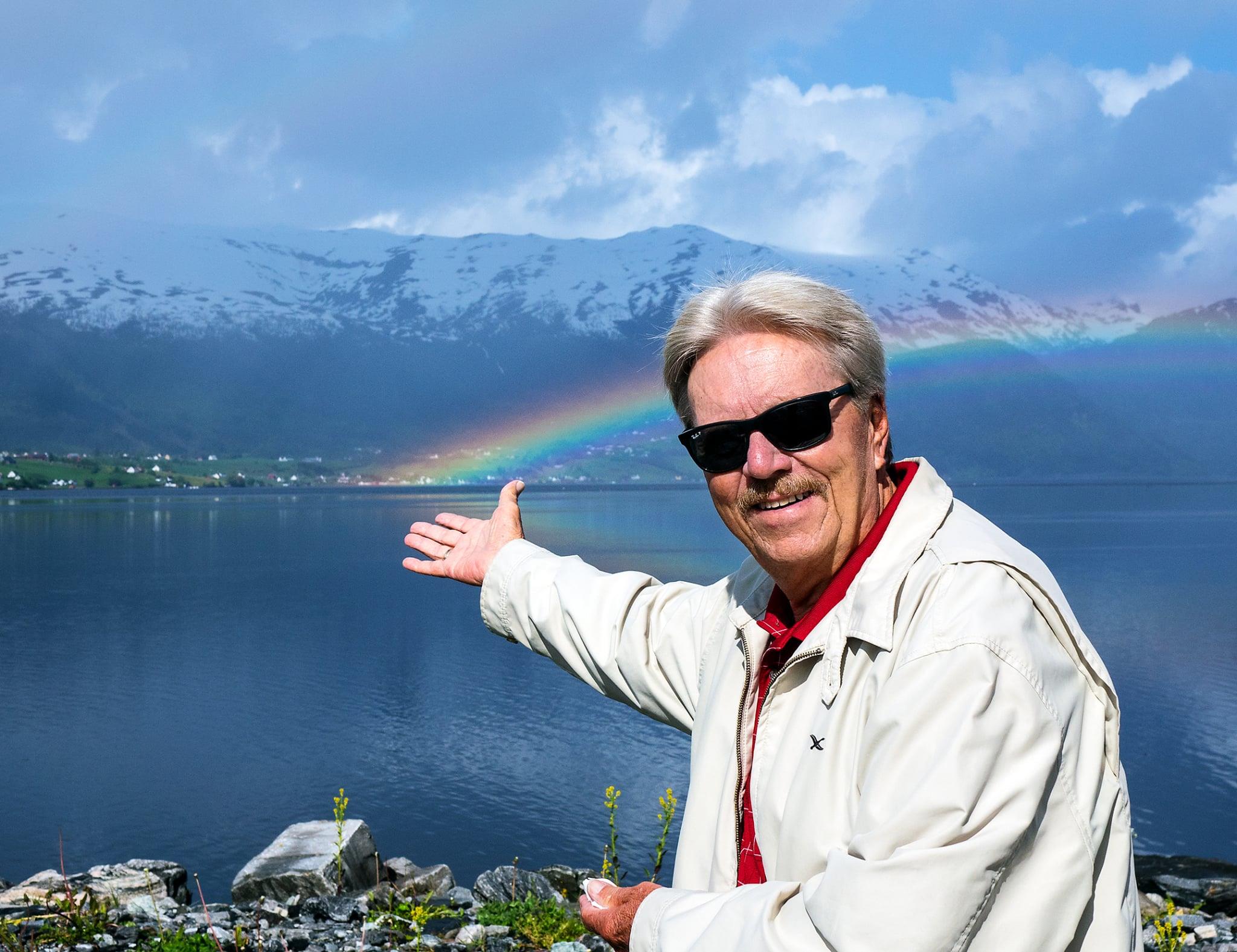 A man in sunglasses with a rainbow in the background