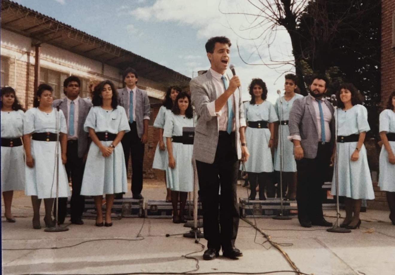 A man singing into a microphone with a group of people in the background