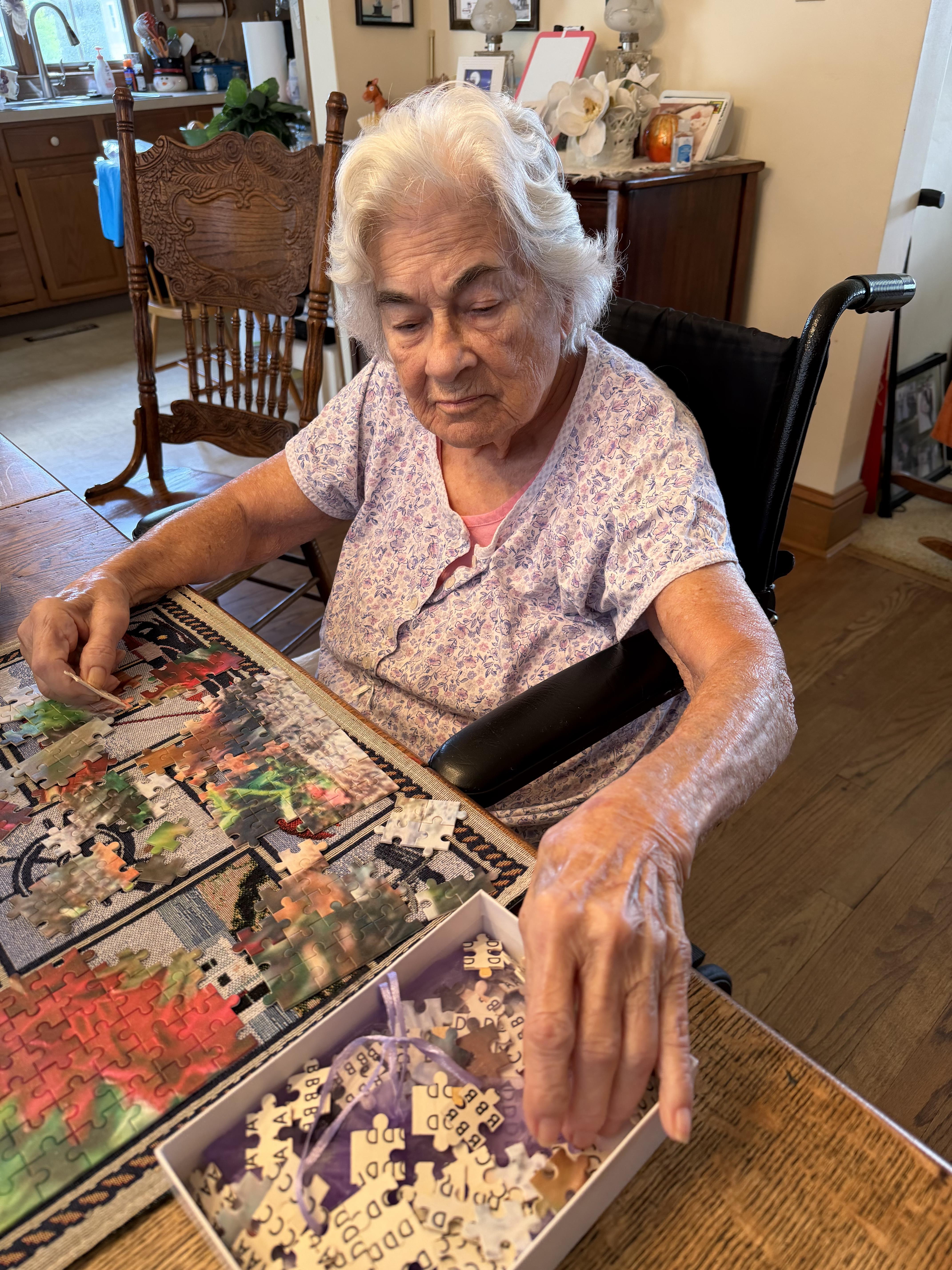 An old woman sitting at a table with a puzzle