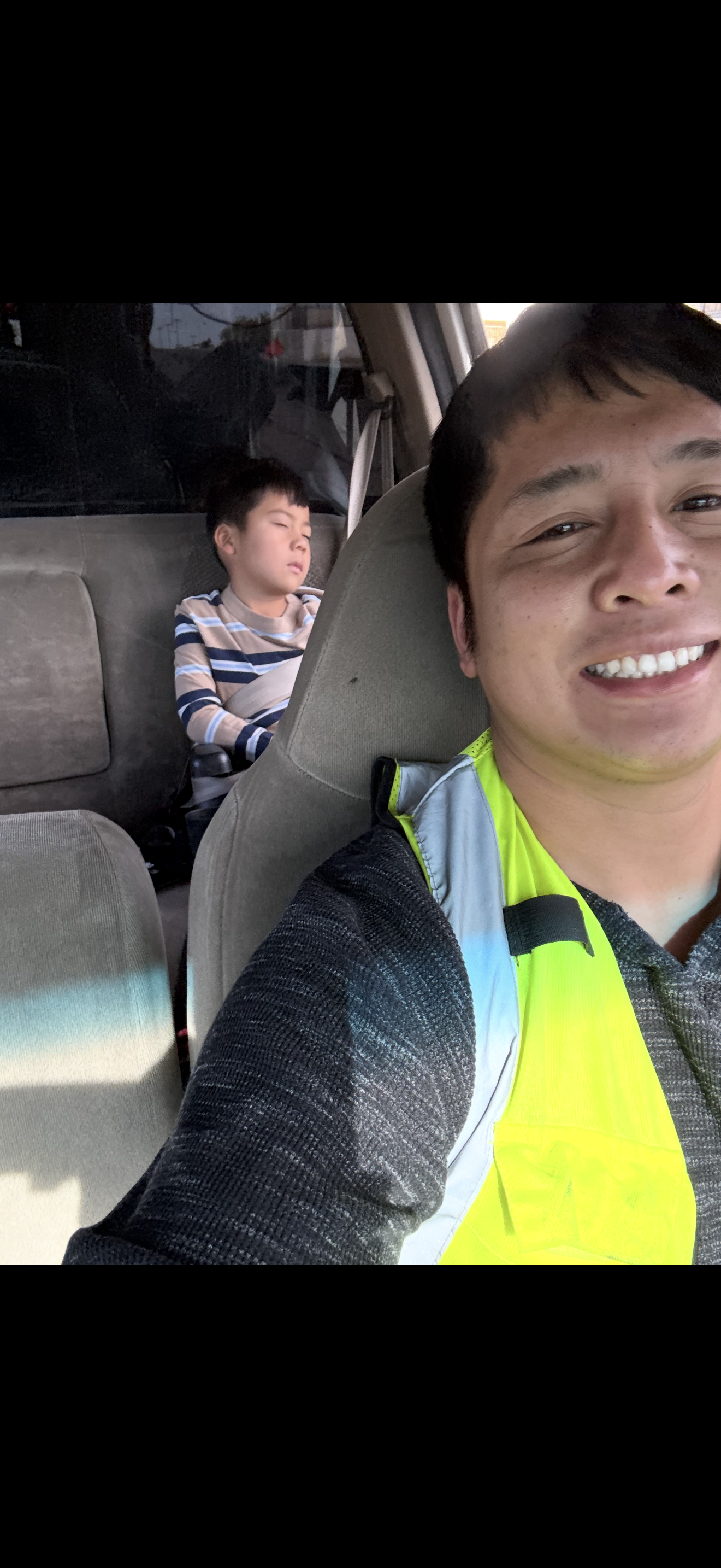 A selfie of a man in a car with another man sleeping
