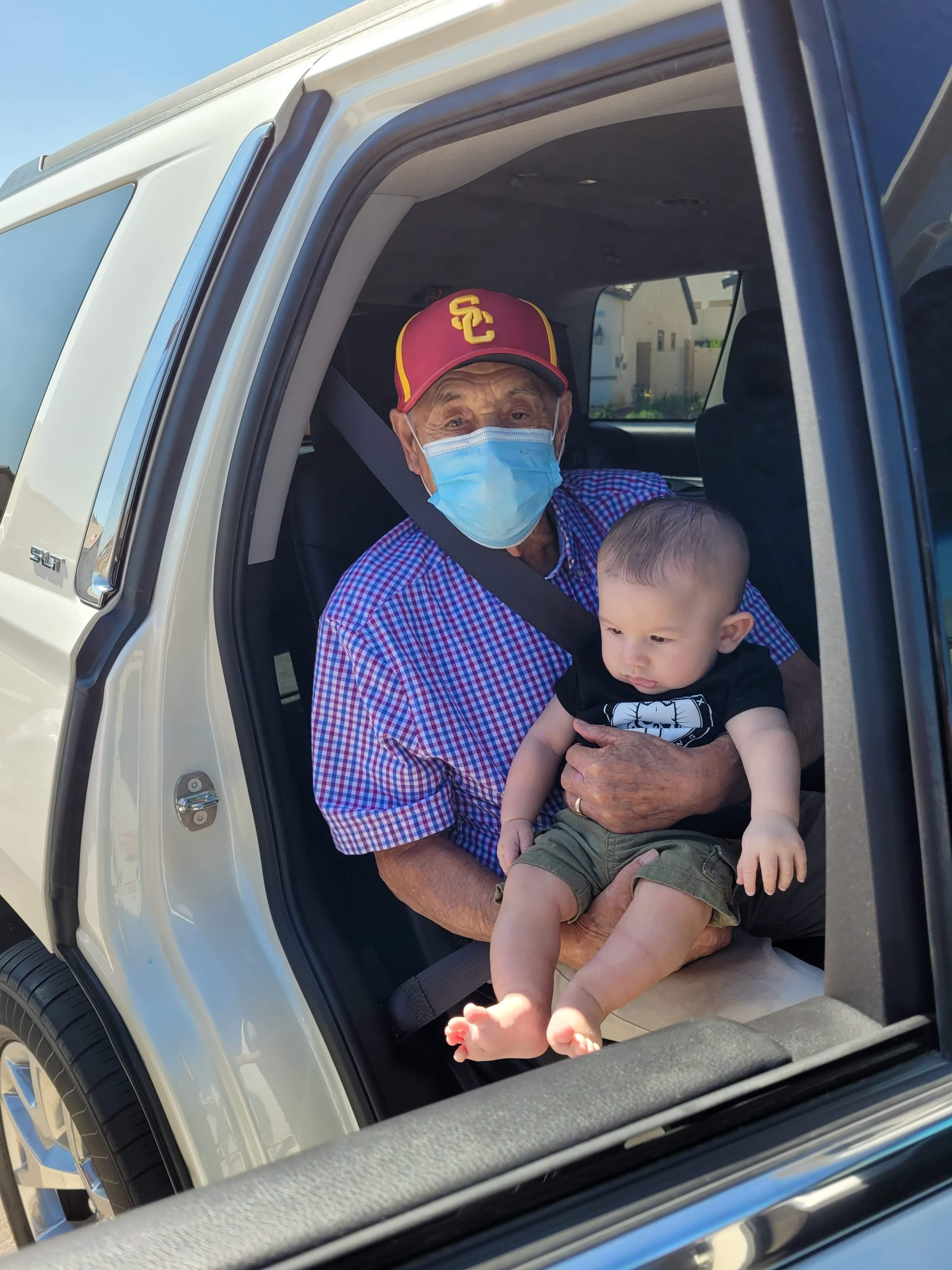 An old man with a face mask sitting in a car with a baby