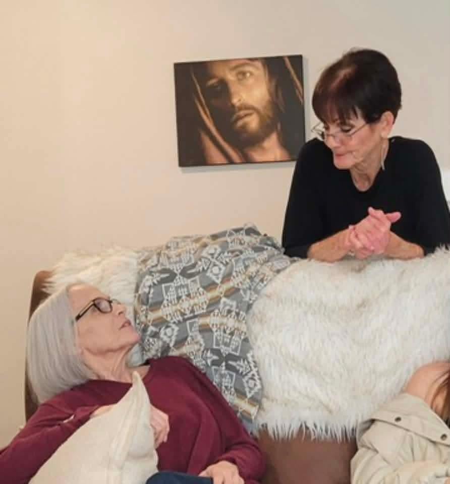 A woman sitting on a couch with a woman in a bed