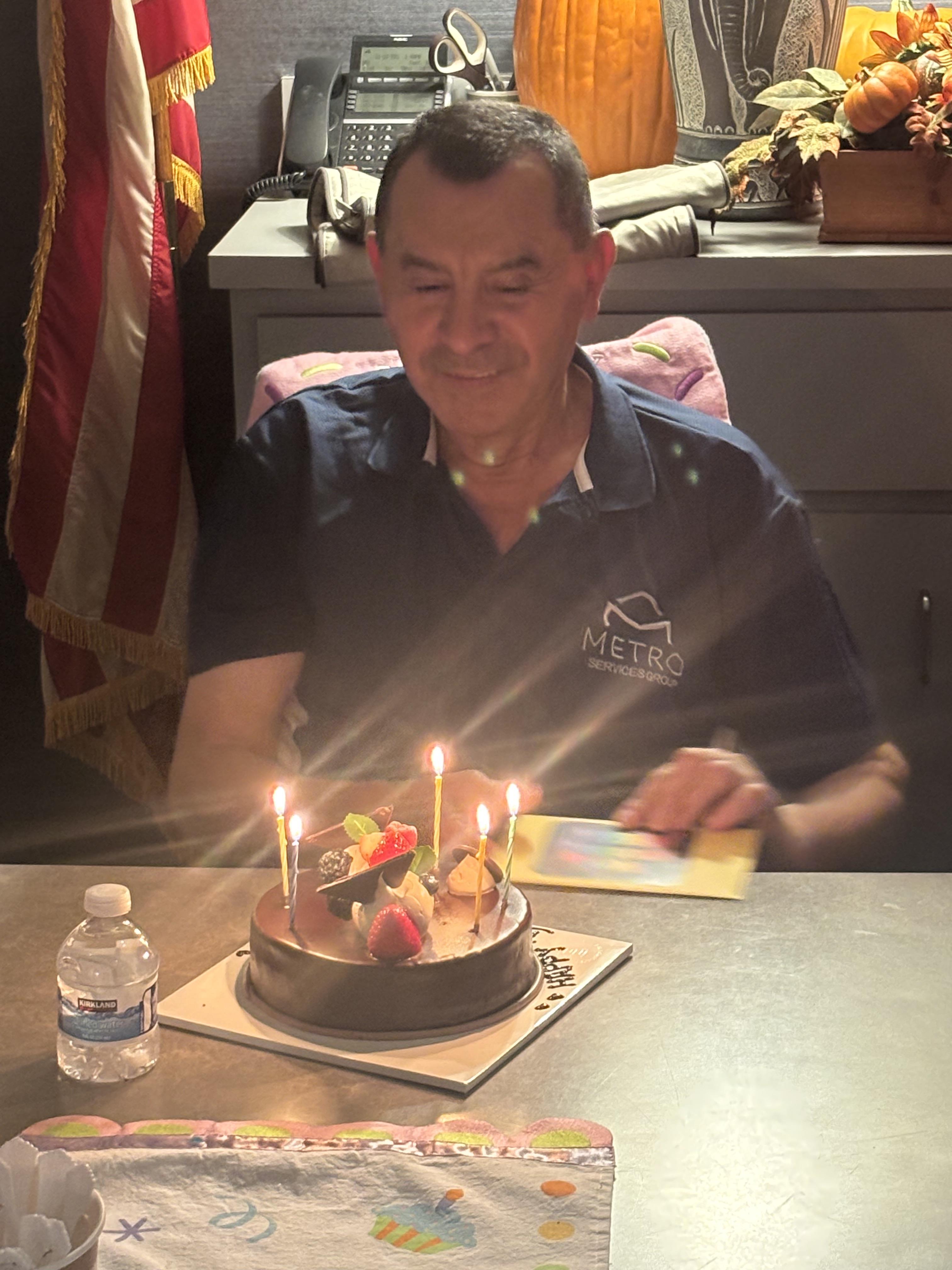 A man sitting at a table with a cake with lit candles