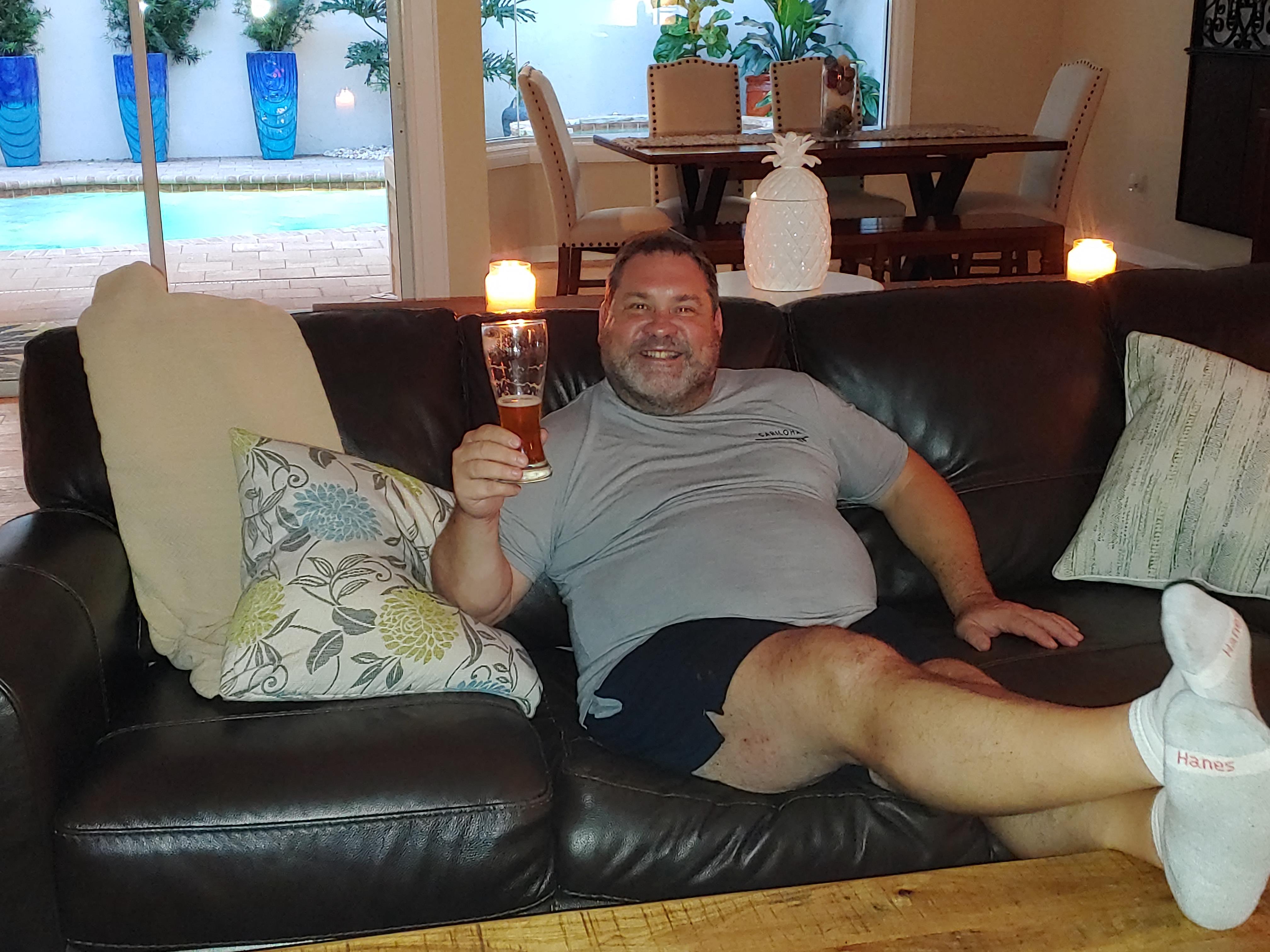 A man lying on a couch holding a glass of beer