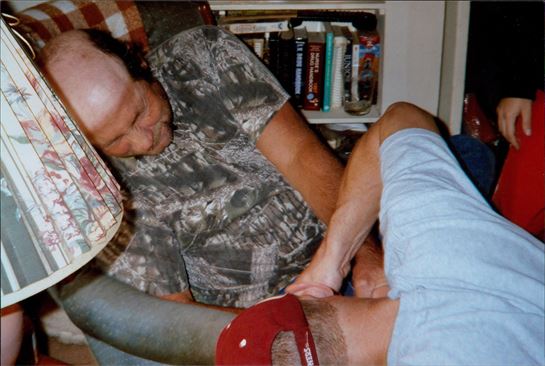 A man lying in a chair holding another man's head