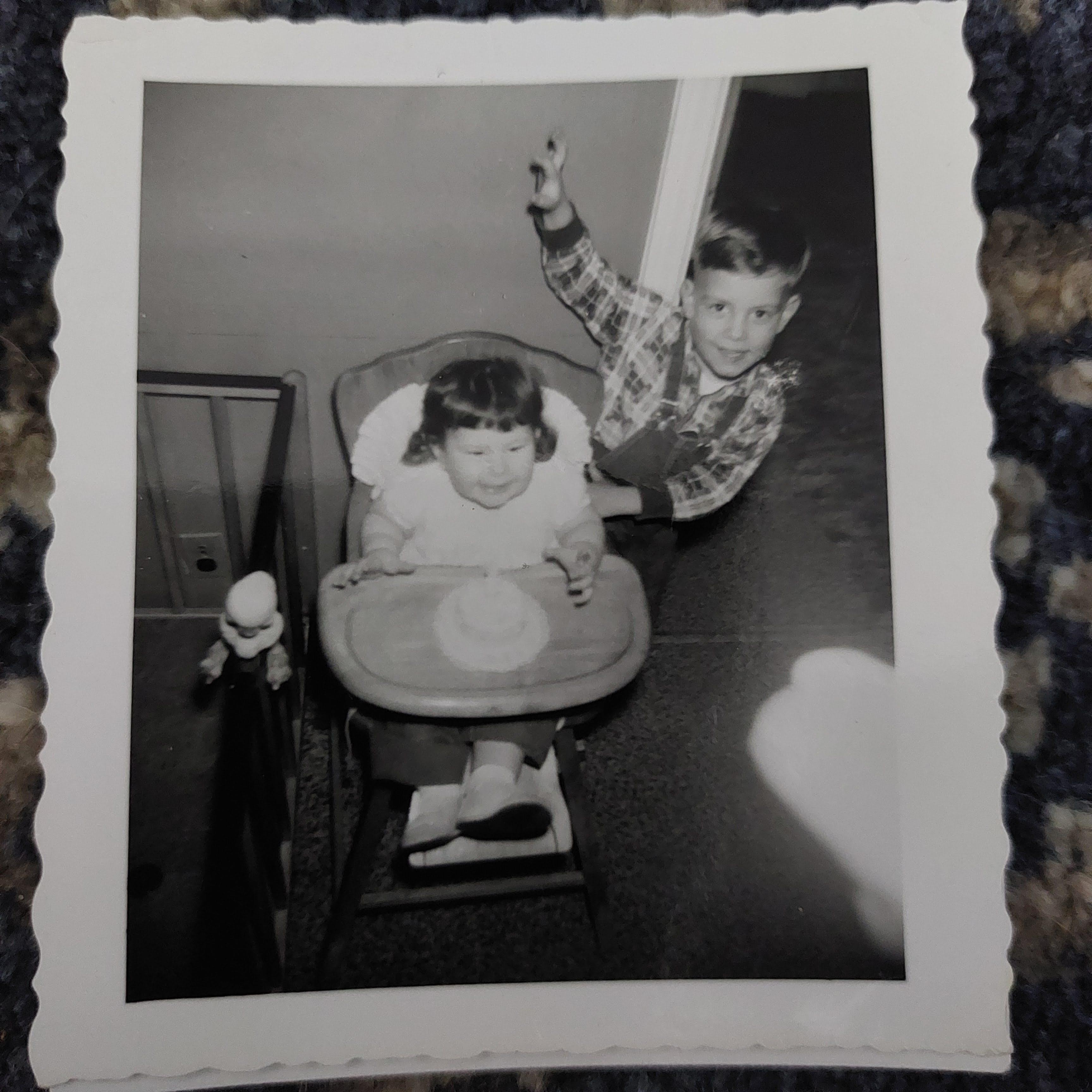 A boy pointing at a baby in a highchair