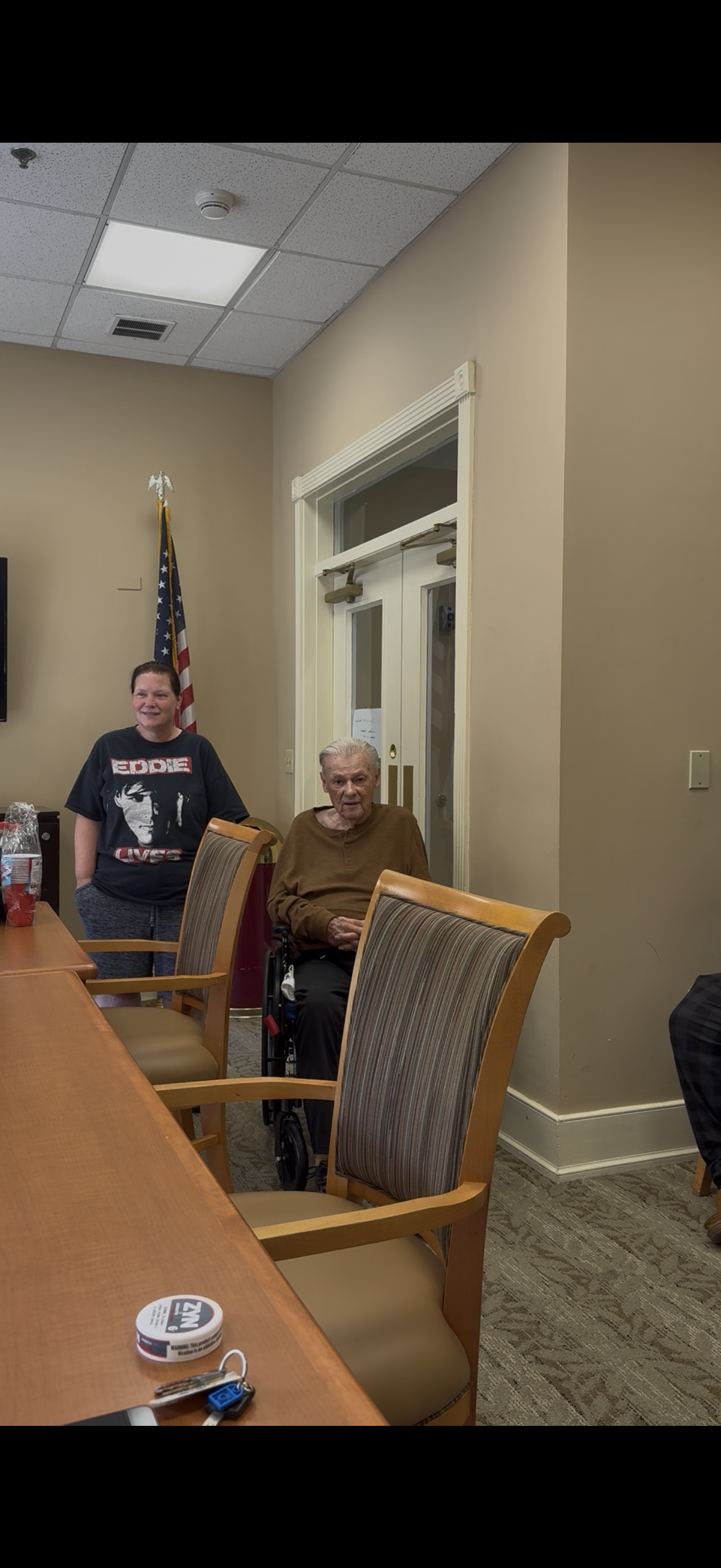 A woman standing next to an old man in a wheelchair