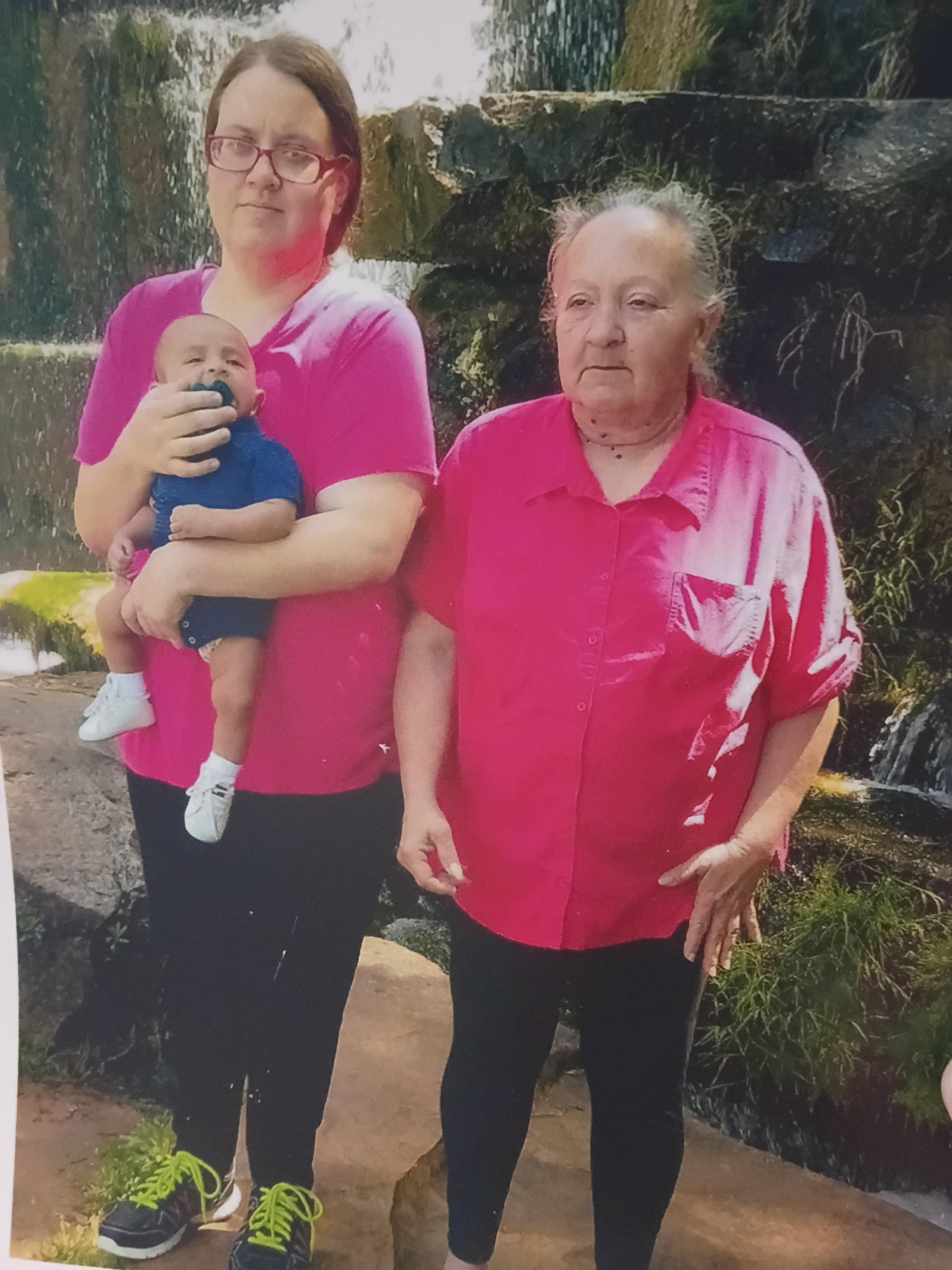 Two women in pink shirts holding a baby