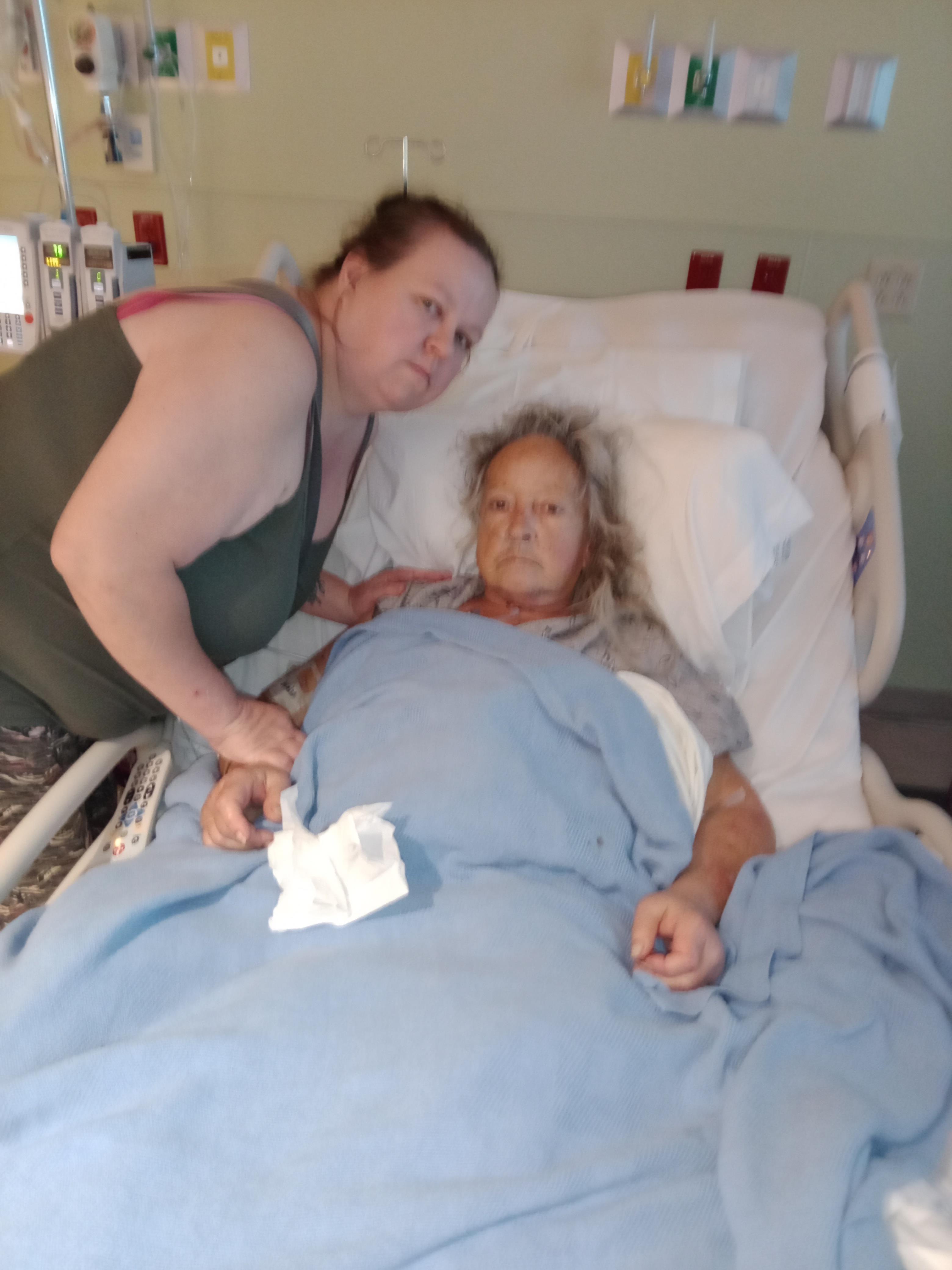 A woman standing next to a woman lying in a hospital bed