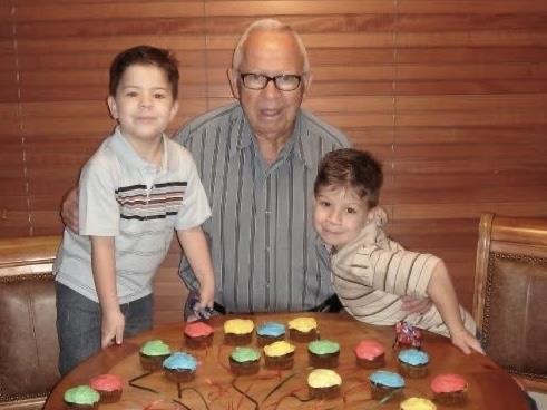 A man and two boys standing in front of a table with cupcakes