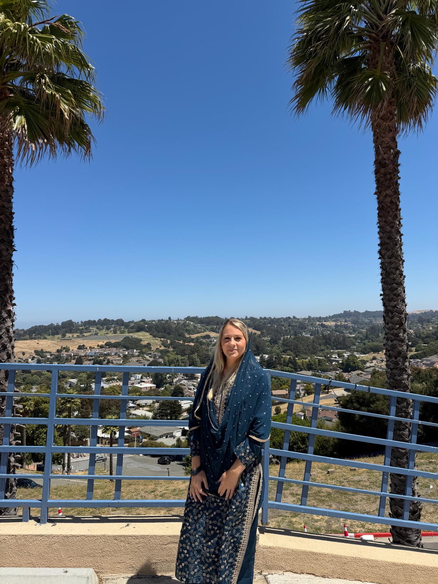 A woman standing on a railing with palm trees and a city in the background