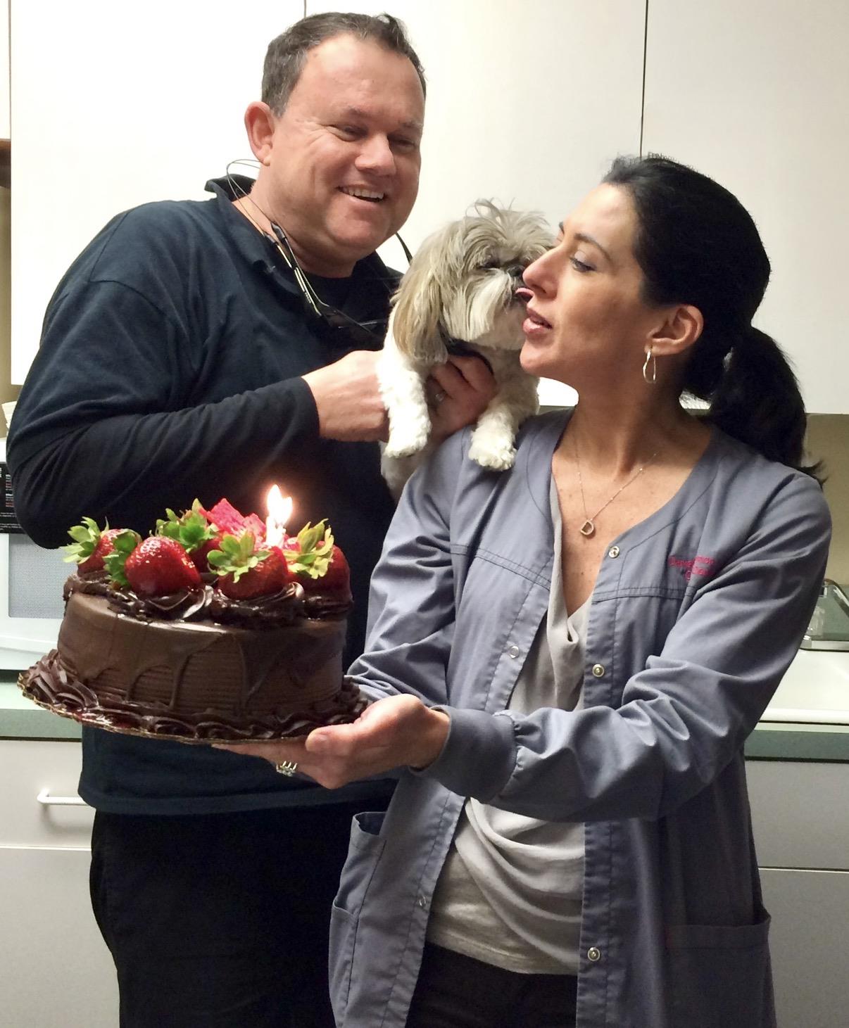 A man and woman holding a cake with a dog